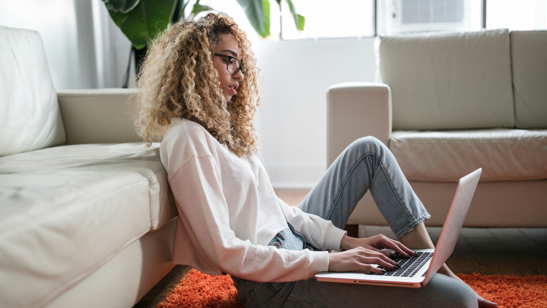 woman sitting on floor and leaning on couch using laptop