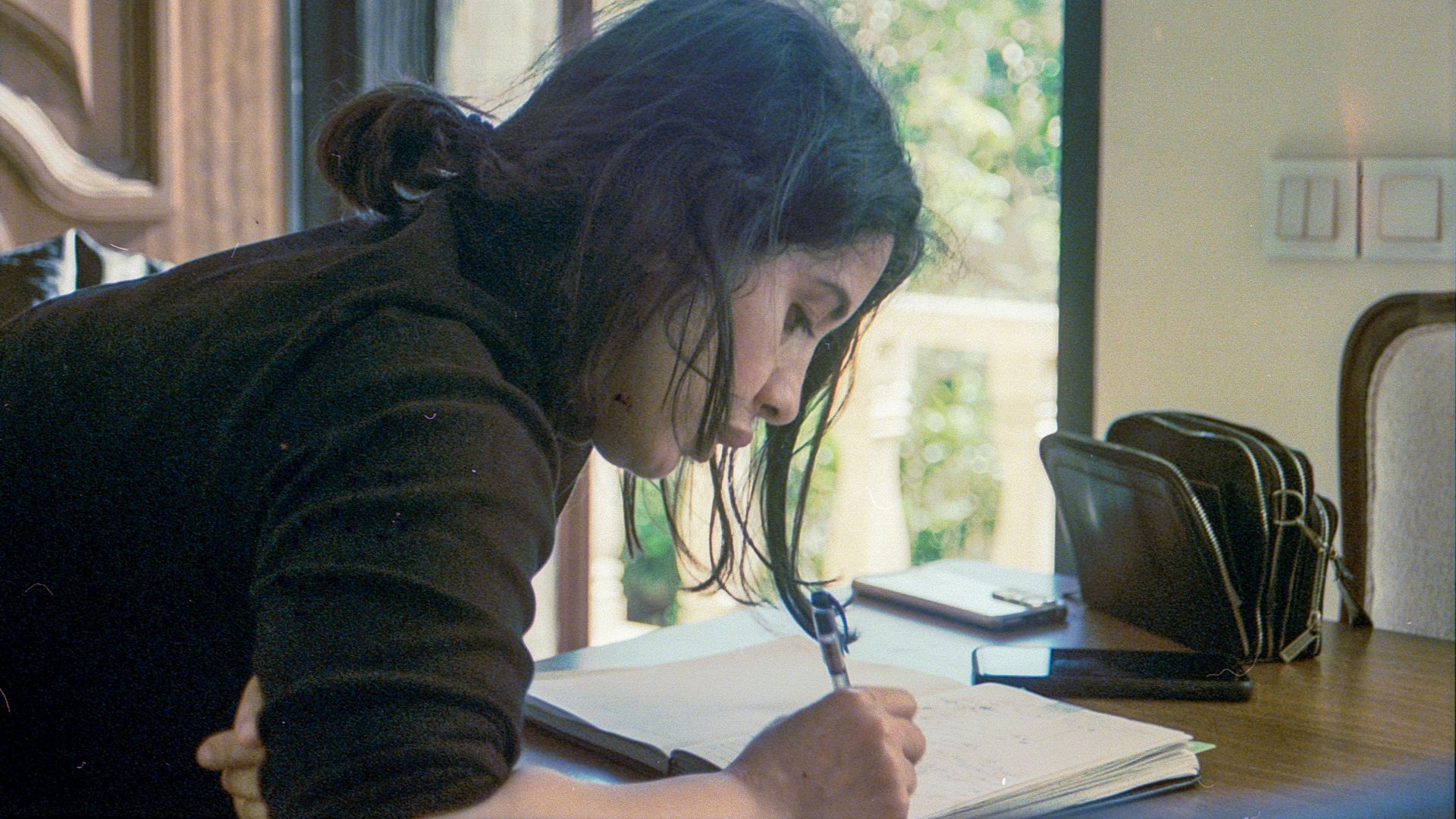 A woman writes in a notebook at a table.