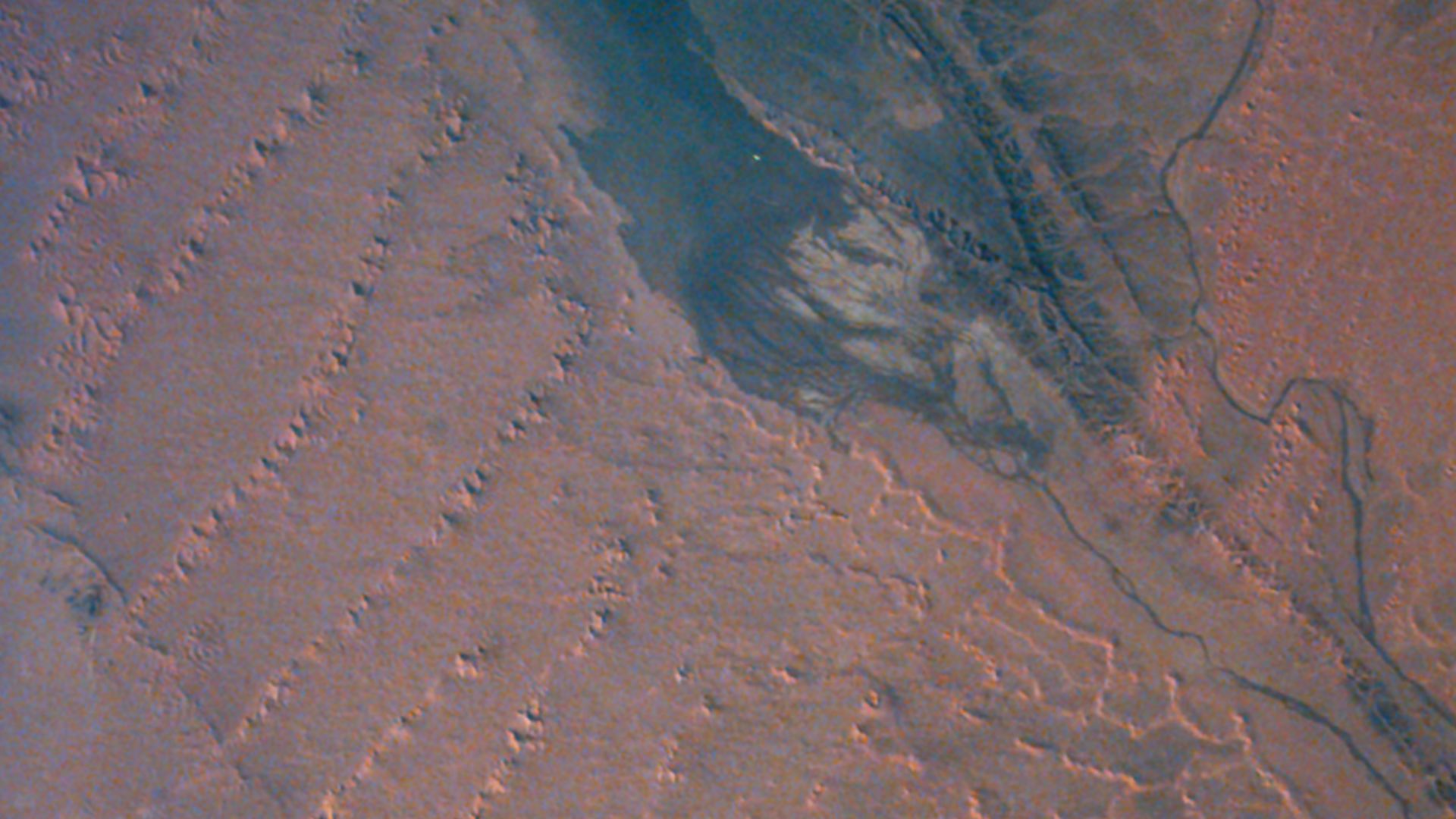 Gemini 7 photograph of the Sahara desert southeast of Bechar in Western Algeria. The lower and left portions of the image show dunes, long ridges 8 to 16 km (5 to 10 miles) apart, 150 to 250 m (500 to 800 ft) high, and hundreds of km long. A wadi, or stream bed which is usually dry, the Oued Saoura, is at the upper right of the image, and is filled with water from a recent rain. To the left of it is a recently formed ephemeral lake. North is up. (Gemini 7, S65-63830)
Location & Time Information
Date/Time (UT): 1965-12-05 T 19:32
Distance/Range (km): 218
Central Latitude/Longitude (deg): +31.,357.

Orbit(s): 13