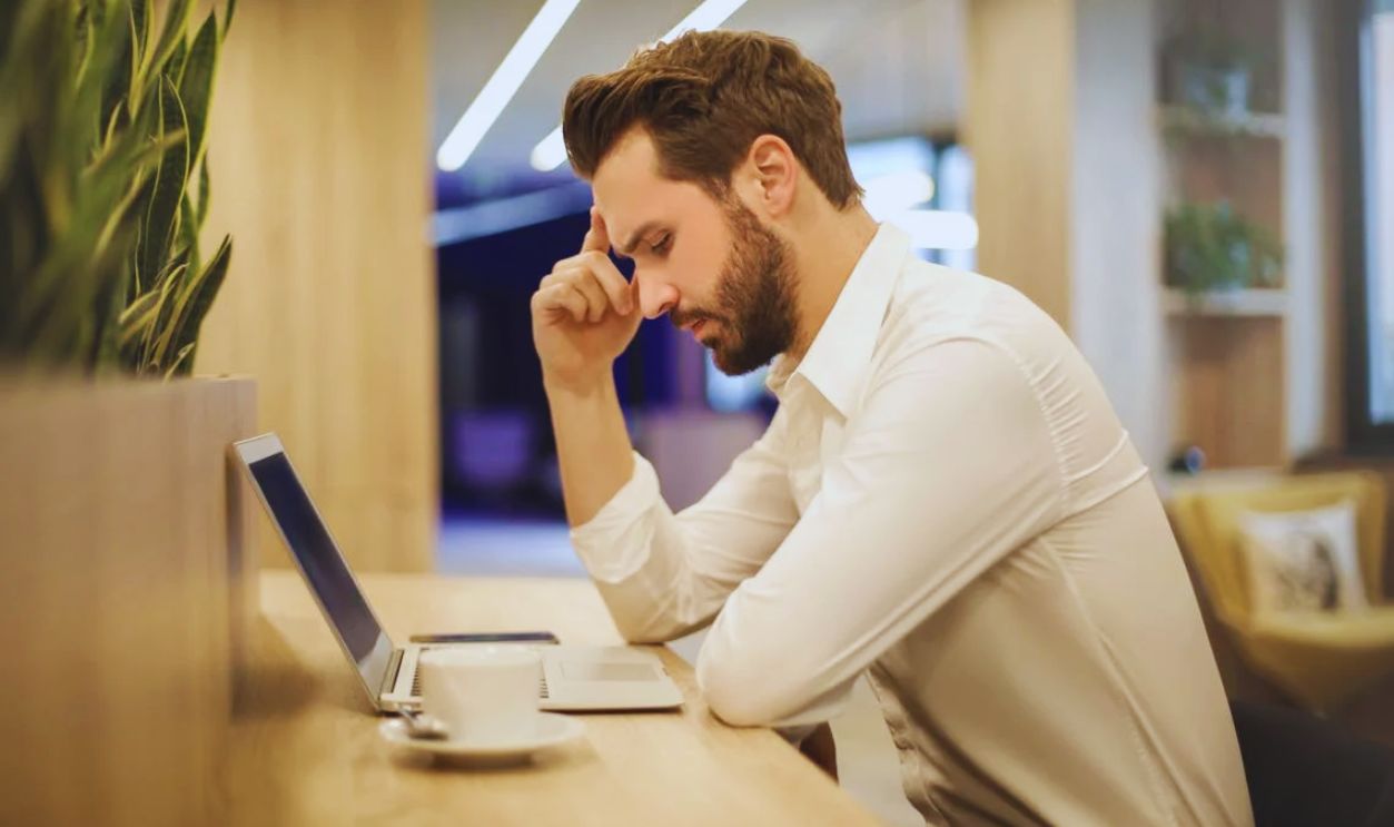 Man With Hand on Temple Looking at Laptop