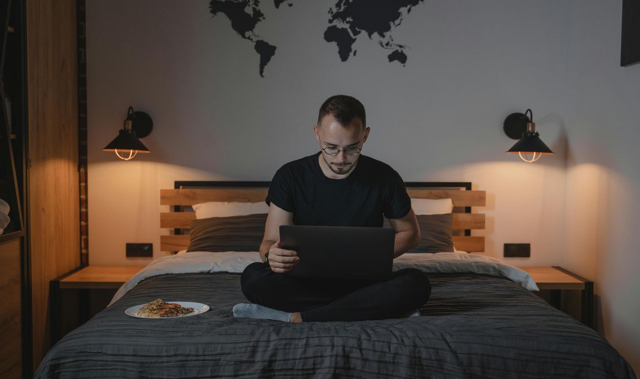 A Man Using a Laptop while Sitting on a Bed