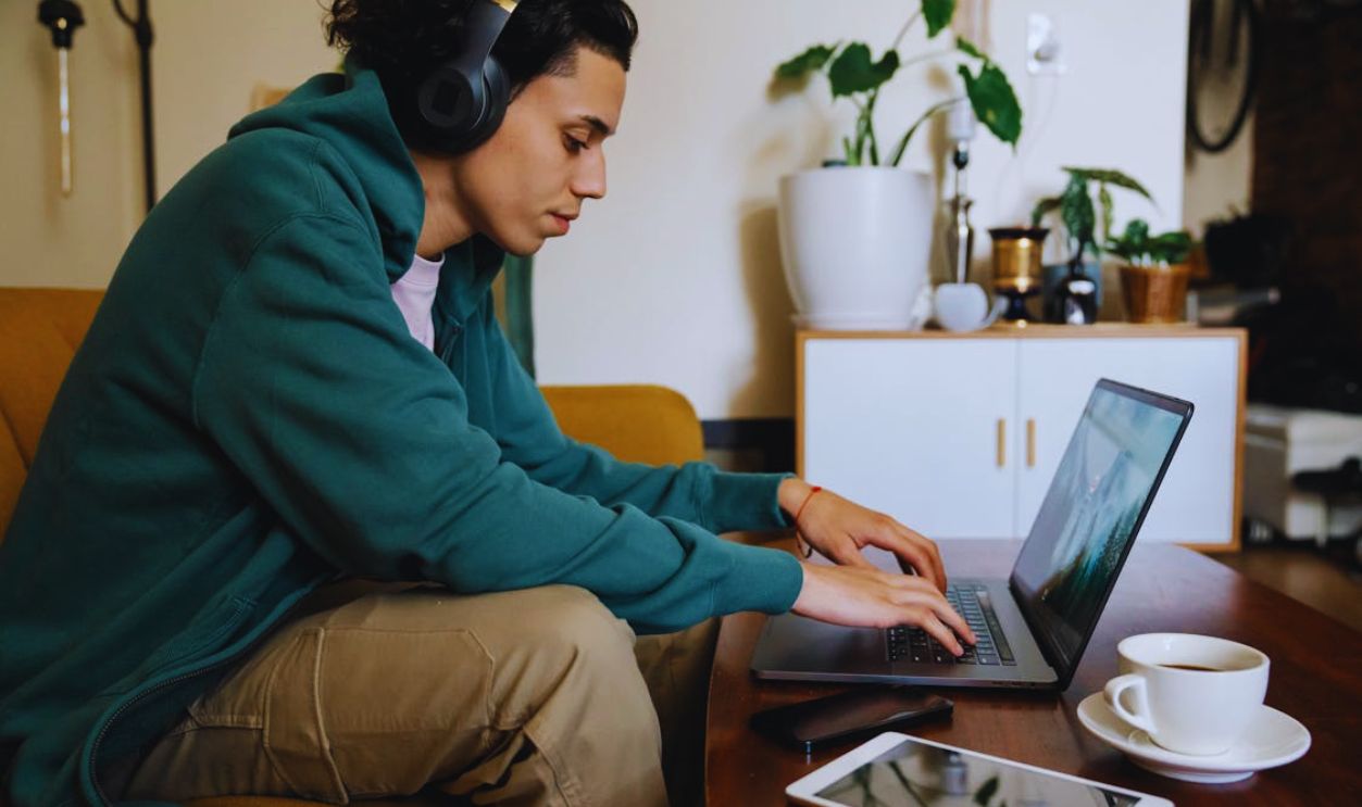 Ethnic freelancer in headphones typing on laptop at home