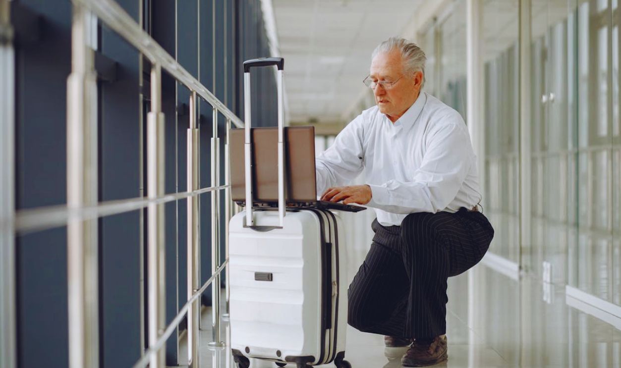 Concentrated man using laptop on baggage in airport corridor
