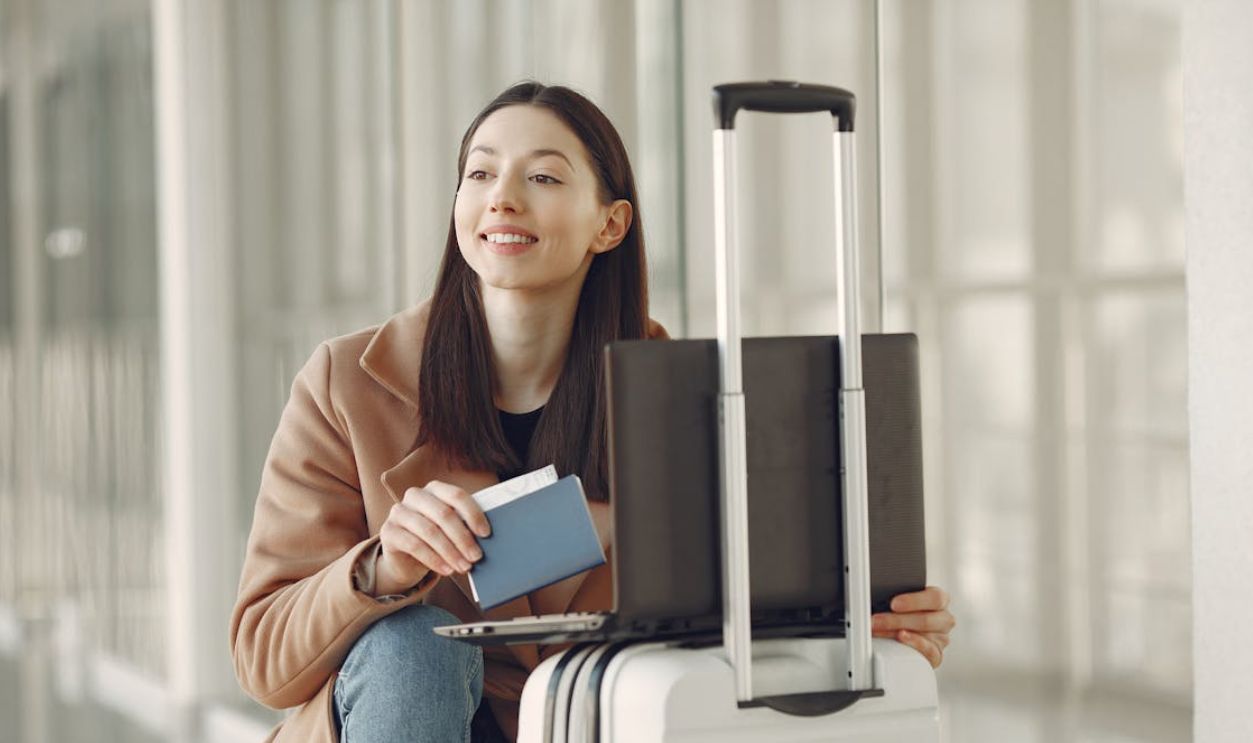 Positive woman with passport using laptop on luggage in airport