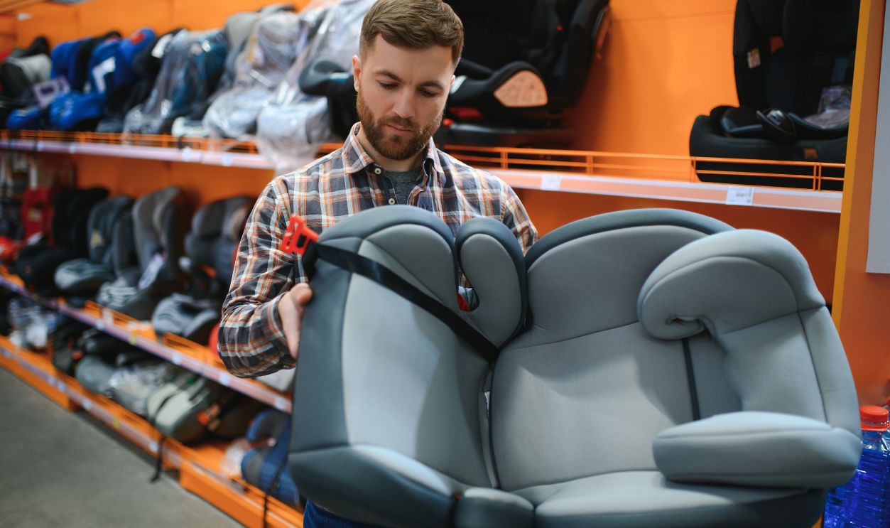 Young father with choosing car seat in store of children's goods.
