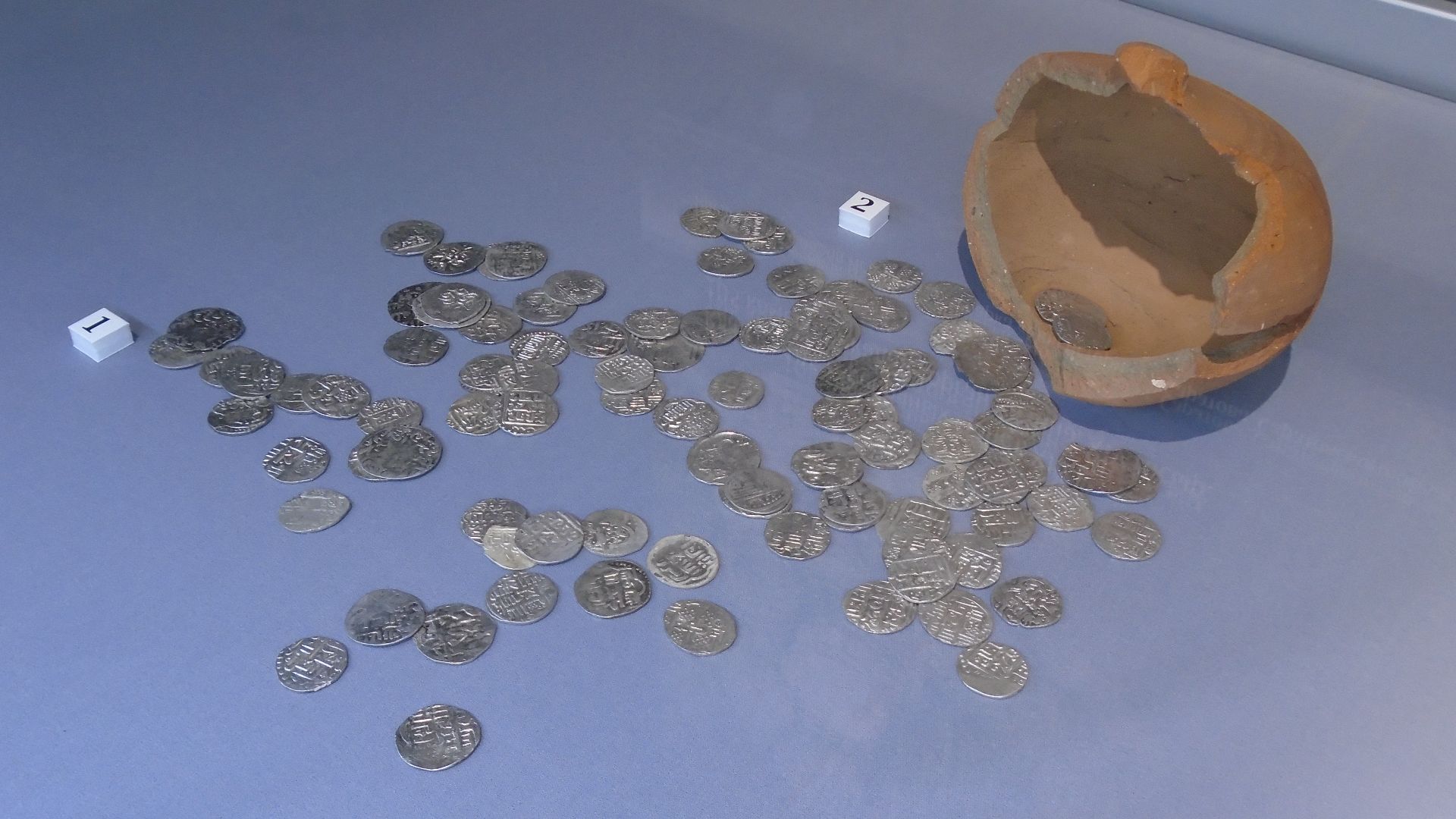 Клад из 105 серебряных монет и красноглиняная копилка. Увекское городище, XIII-XIV вв. Раскопки Д. А. Кубанкина, 2022 г.  Собрание саратовского исторического парка «Россия — моя история». Выставка «Города не исчезают. История Укека в находках». Музей истории государственности татарского народа и Республики Татарстан.