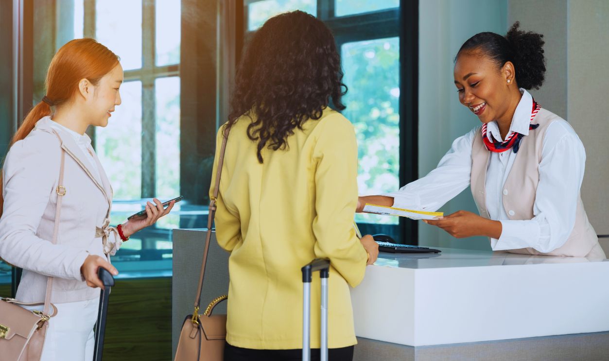 African woman airline ground staff giving boarding pass or ticket to businesswoman passenger at airport check in counter. Business trip concept
