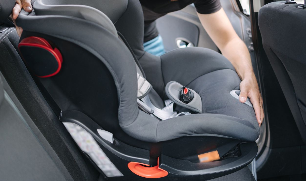 Man installs a child car seat in car at the back seat. Responsible father thought about the safety of his child. Man fasten seat belt on baby car seat