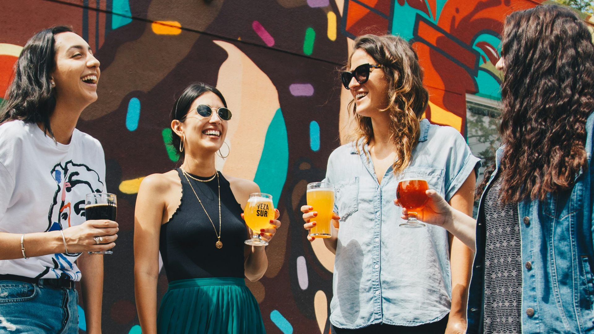 four women holding drinks while laughing together during daytime