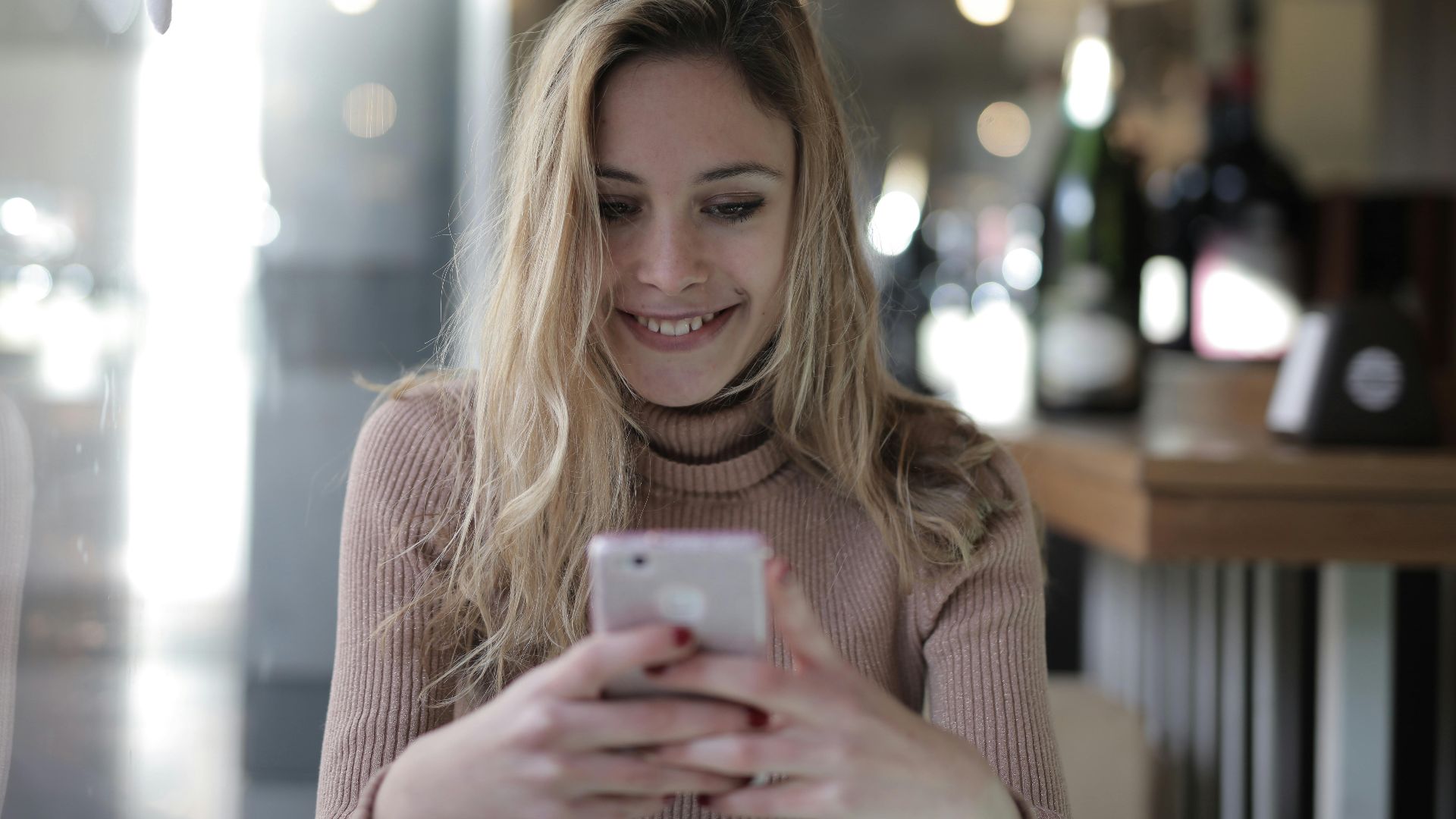 A joyful woman with blonde hair texting on her smartphone in a cozy cafe.