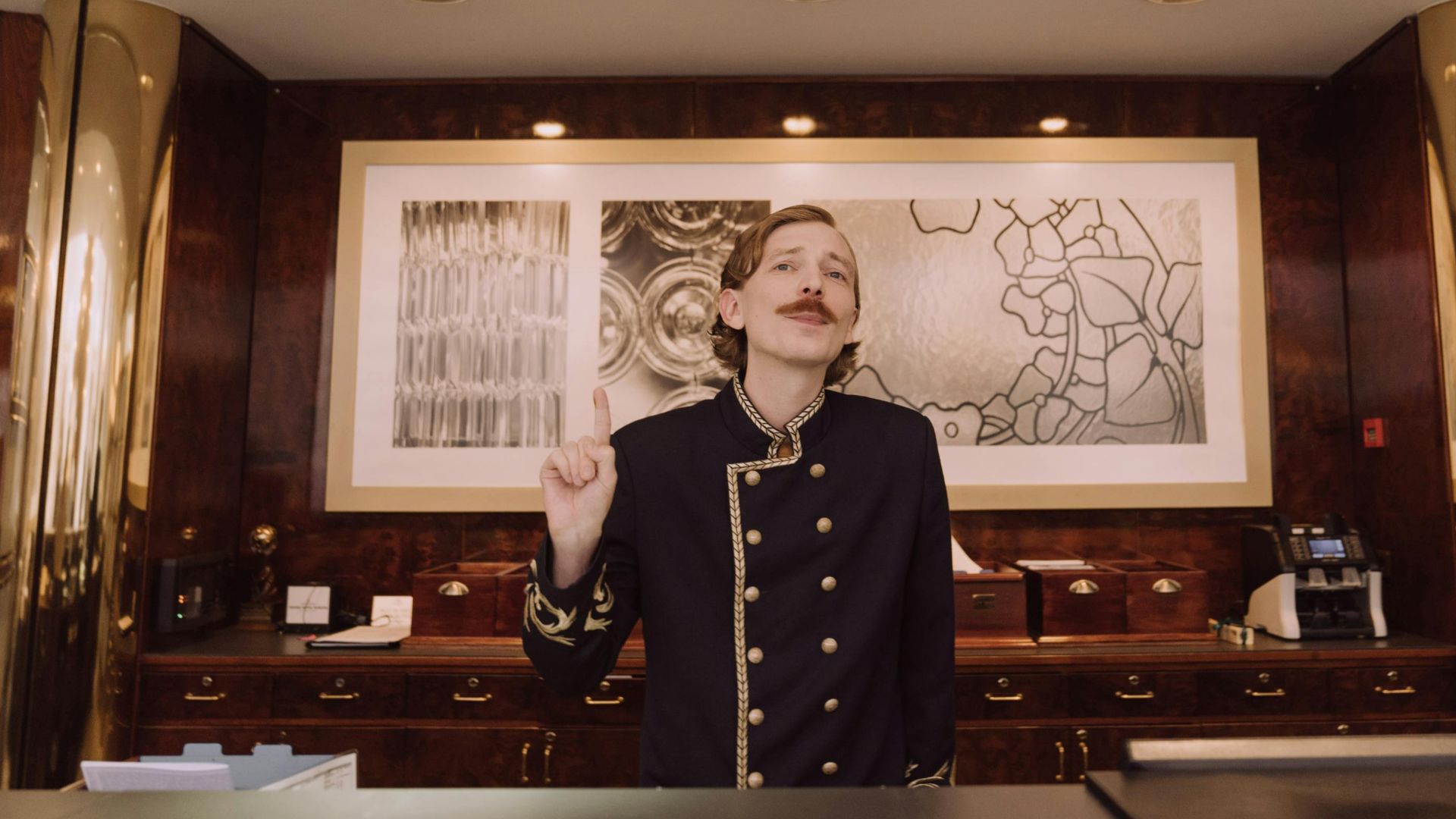 A luxury hotel receptionist in uniform stands behind the opulent front desk, ready to assist guests.