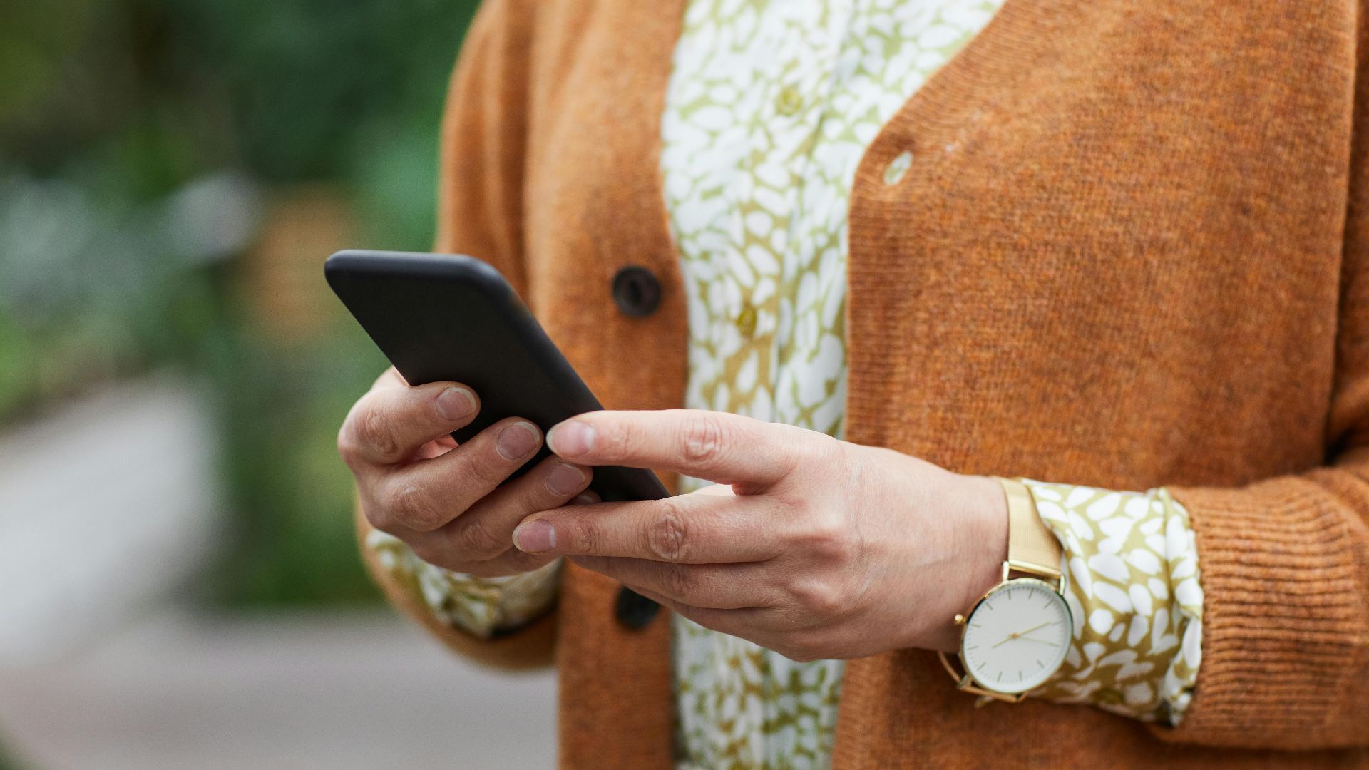 Elderly person's hands holding a smartphone in a casual setting, wearing a watch.