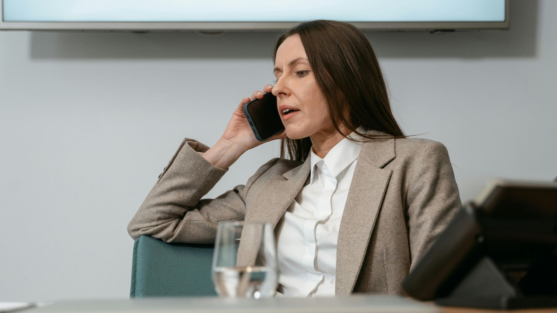 Businesswoman in a blazer making a phone call in an office setting, engaging in a conversation.