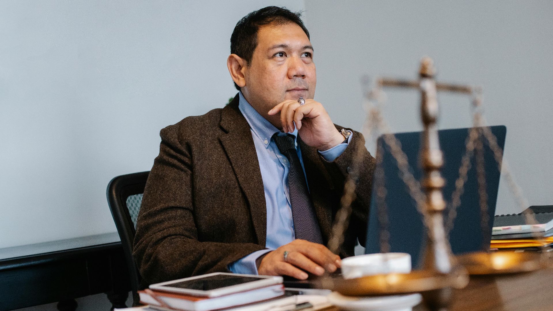 Asian lawyer at work with laptop and legal scales, focused and thoughtful.