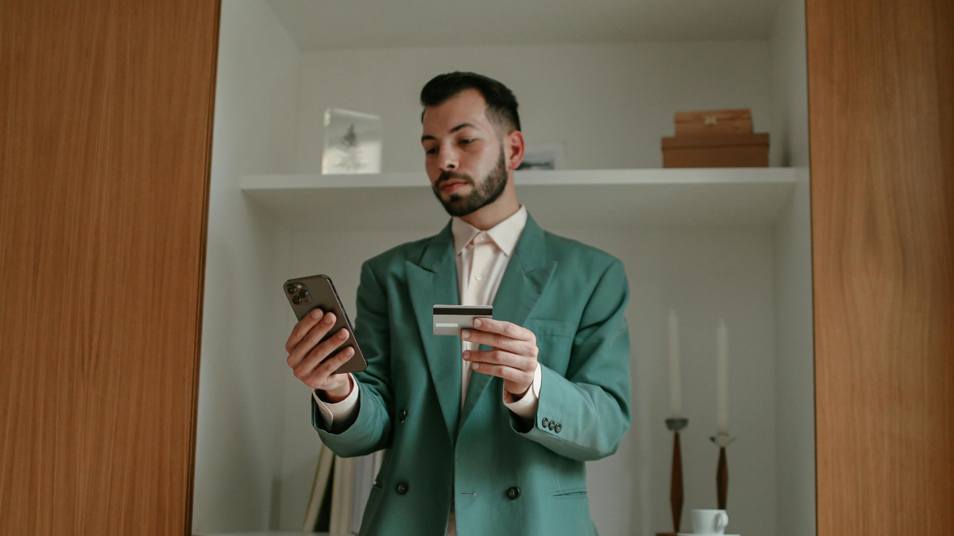 A bearded man in a green suit is using a smartphone and credit card indoors, showcasing modern technology and lifestyle.