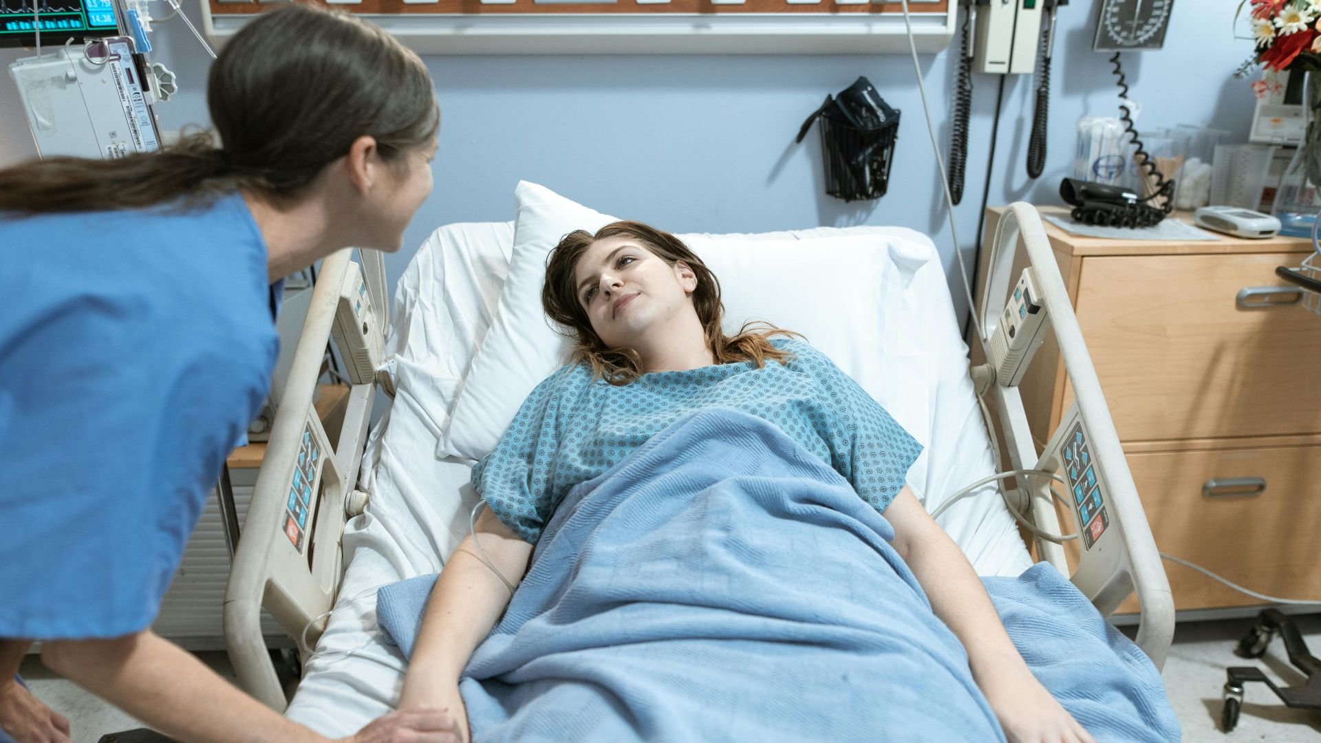 A nurse compassionately holds a patient's hand in a hospital room setting, promoting care and support.