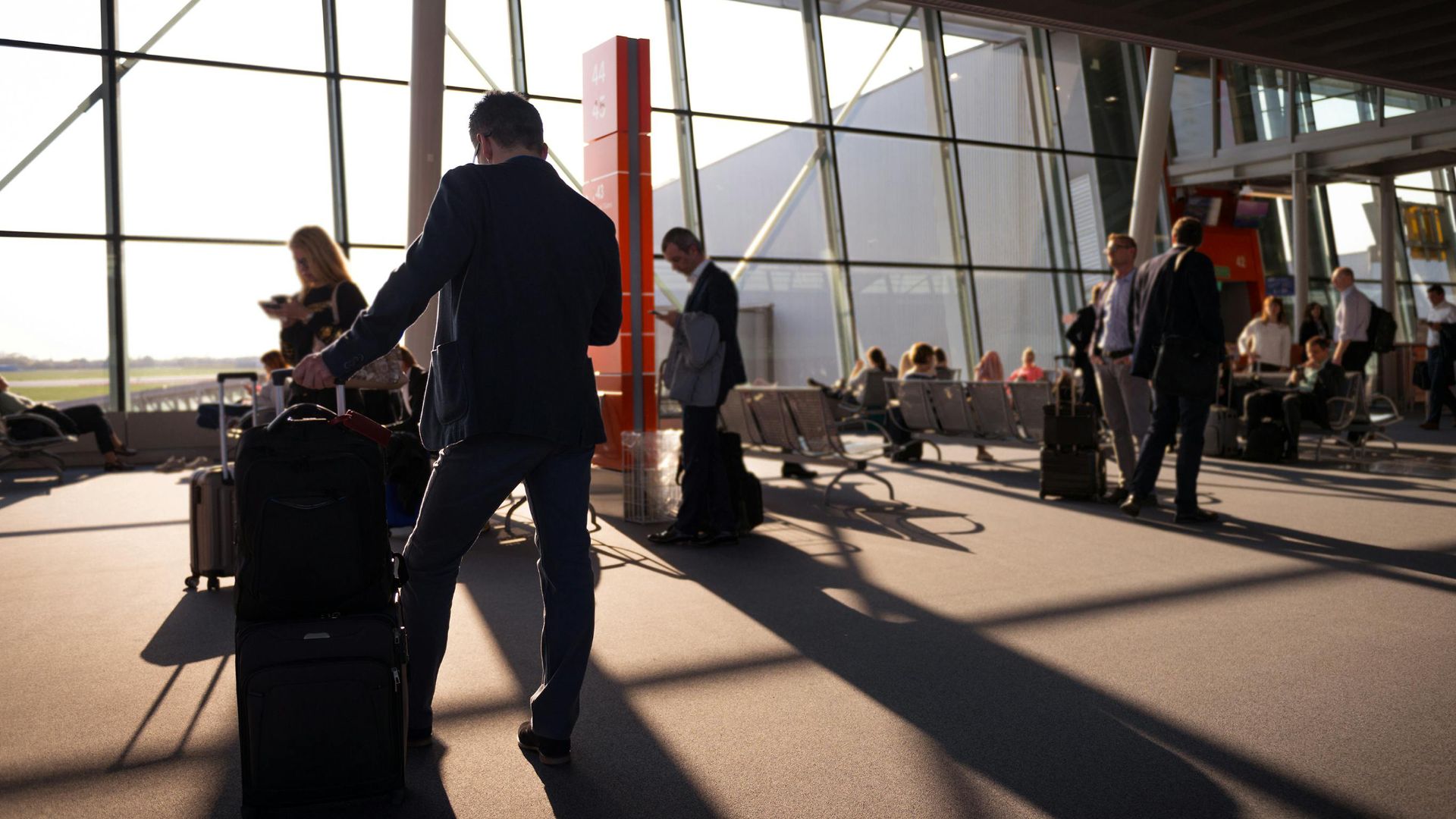 Travelers in a bustling airport terminal with carry-on luggage waiting for departure.