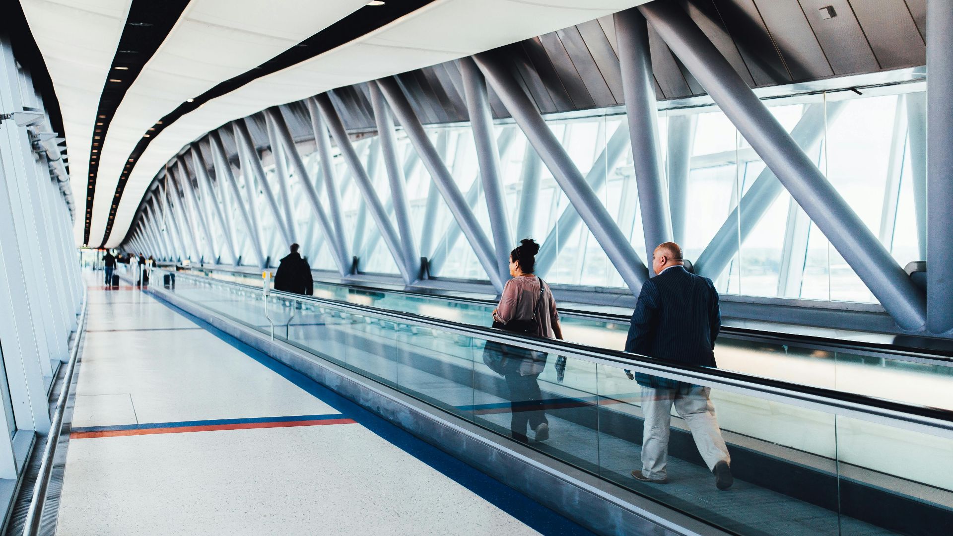 Travelers walking through a bright modern airport corridor with glass walls.