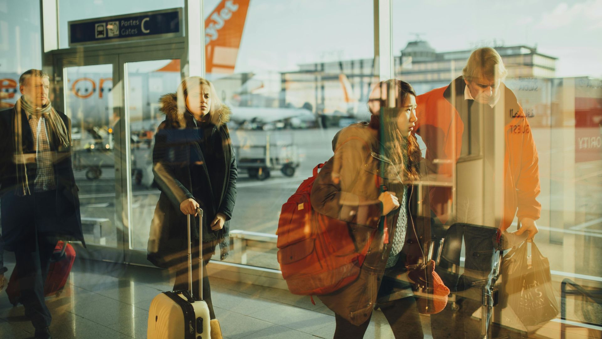 Passengers moving through an airport gate area with visible airplanes outside.