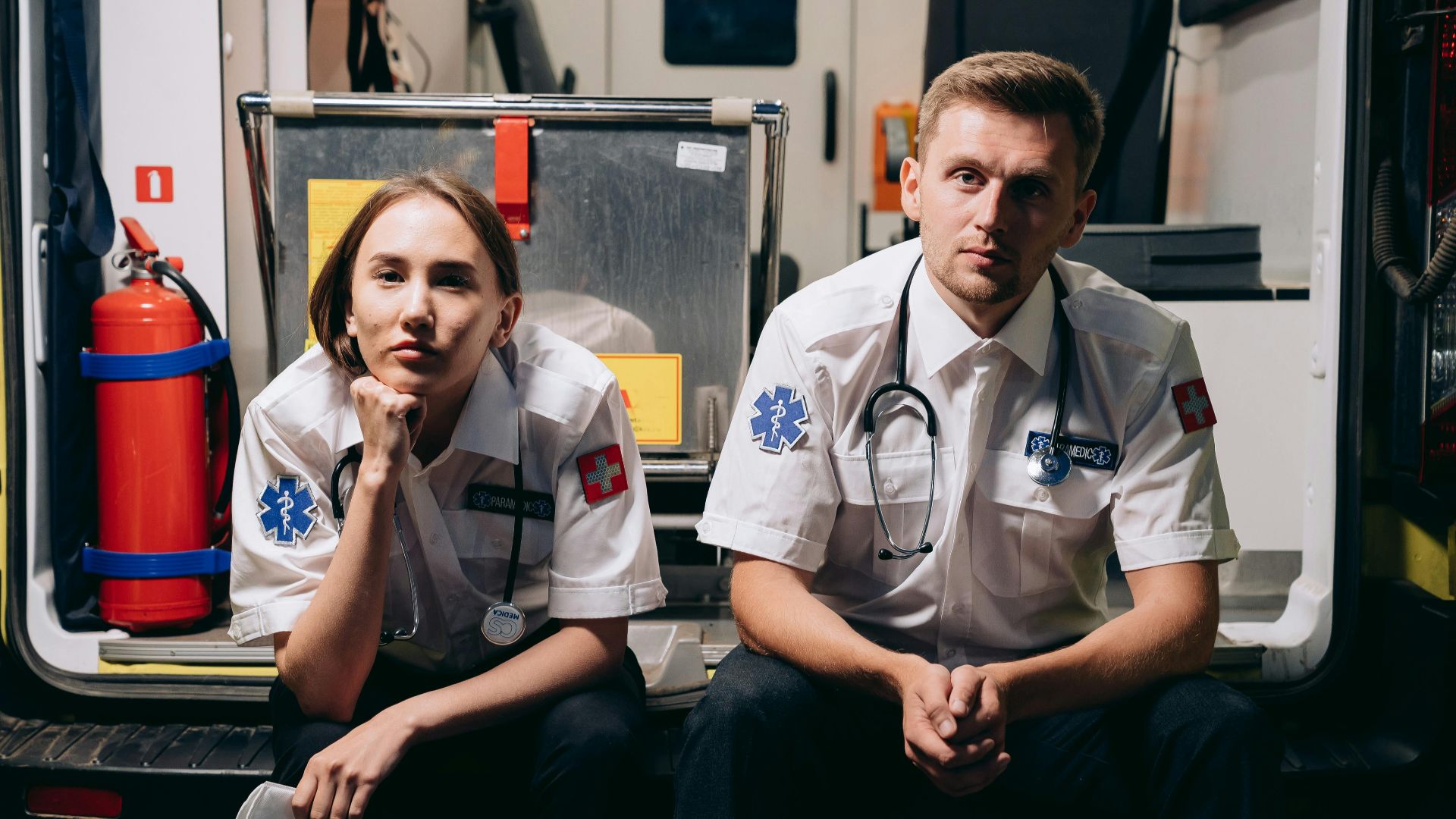 Two paramedics in uniforms sitting inside an ambulance, showcasing teamwork and readiness.