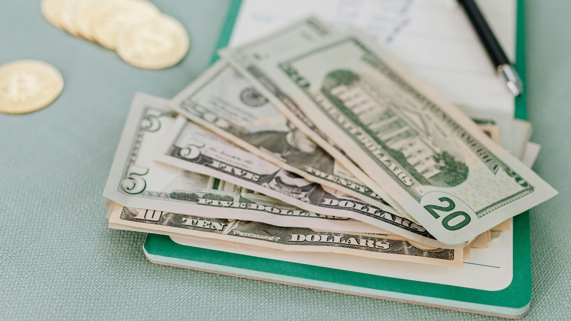 Close-up of American dollar bills and coins on a journal with a pen, representing budget planning.