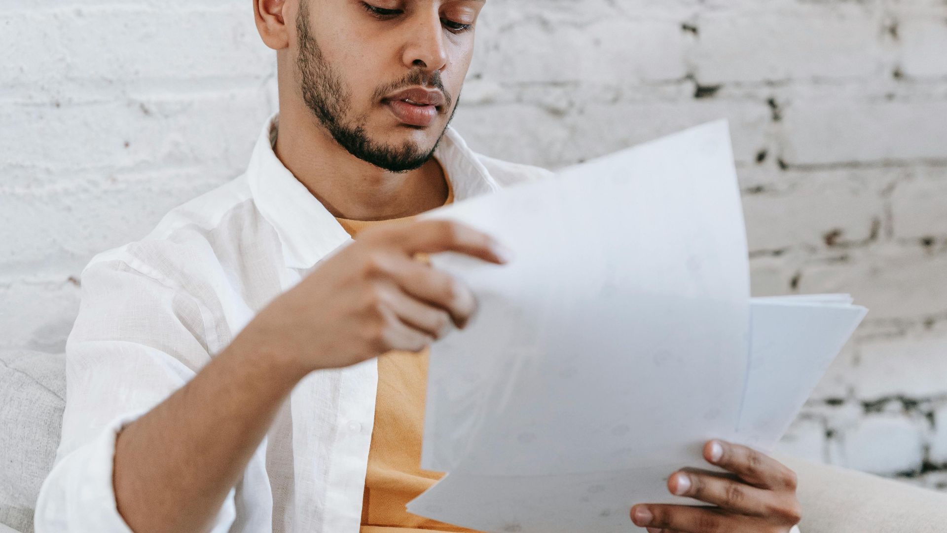 Young man attentively reviewing financial documents at home. Focused on paperwork.