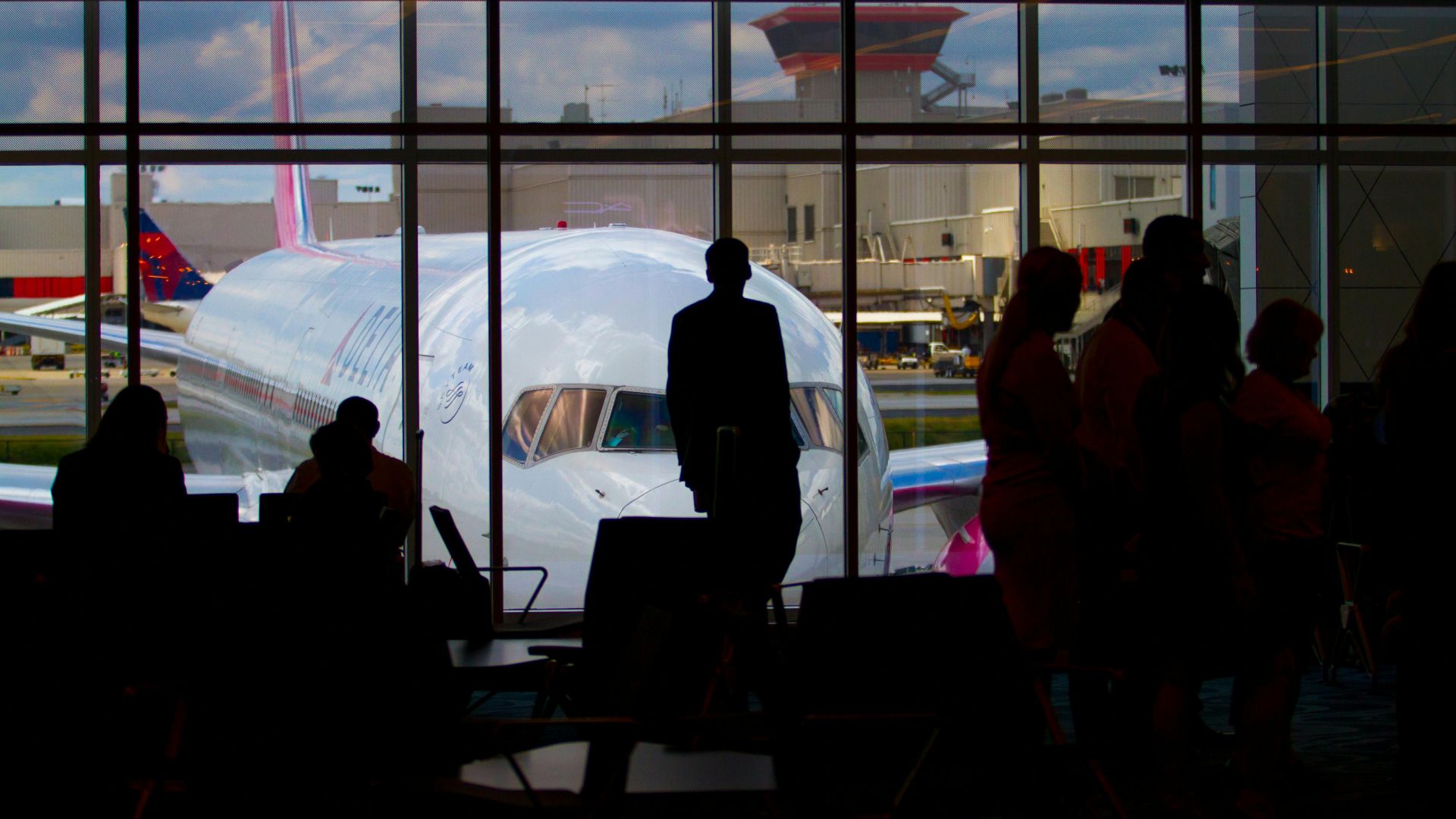 Silhouettes of travelers waiting at an airport terminal with an airplane visible through the window.