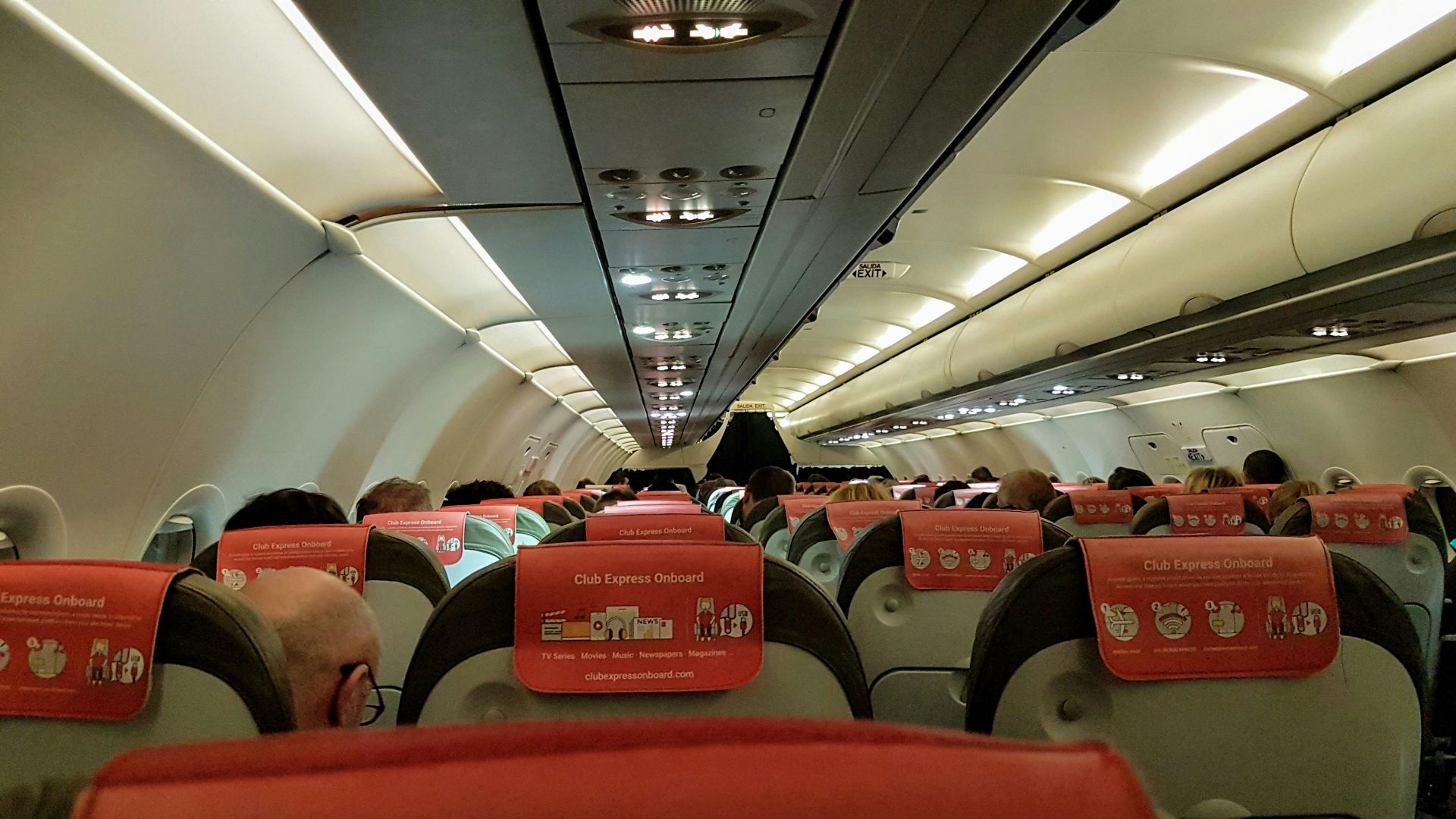 A look inside an airplane cabin filled with seated passengers during a flight.