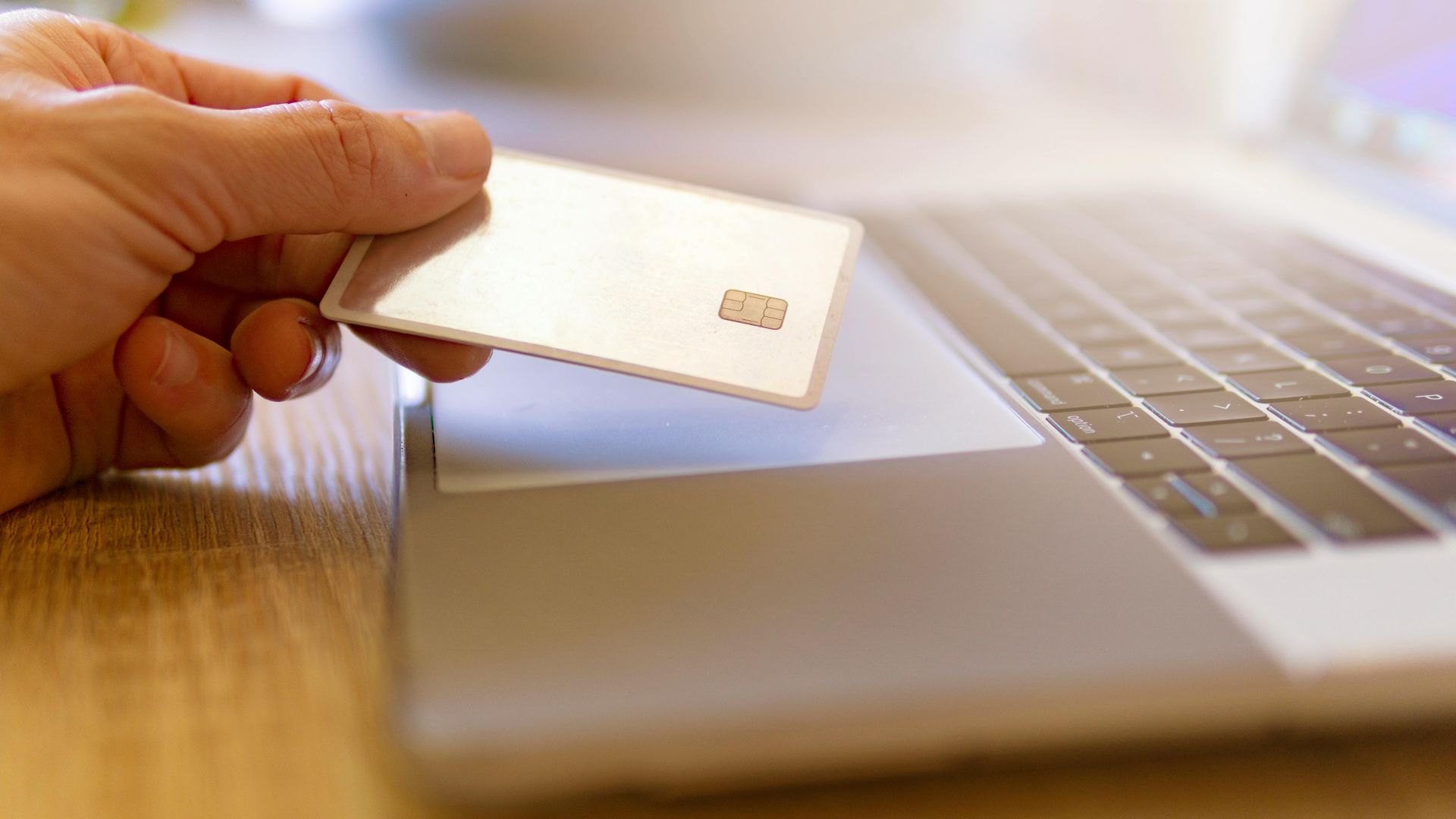 A person holds a credit card near a laptop for online shopping.