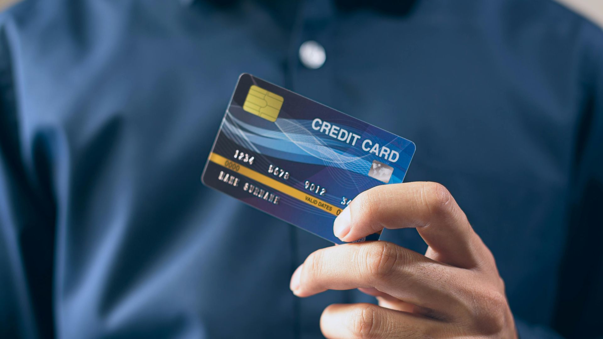 Close-up of a person holding a credit card in a hand, wearing a button-up shirt.