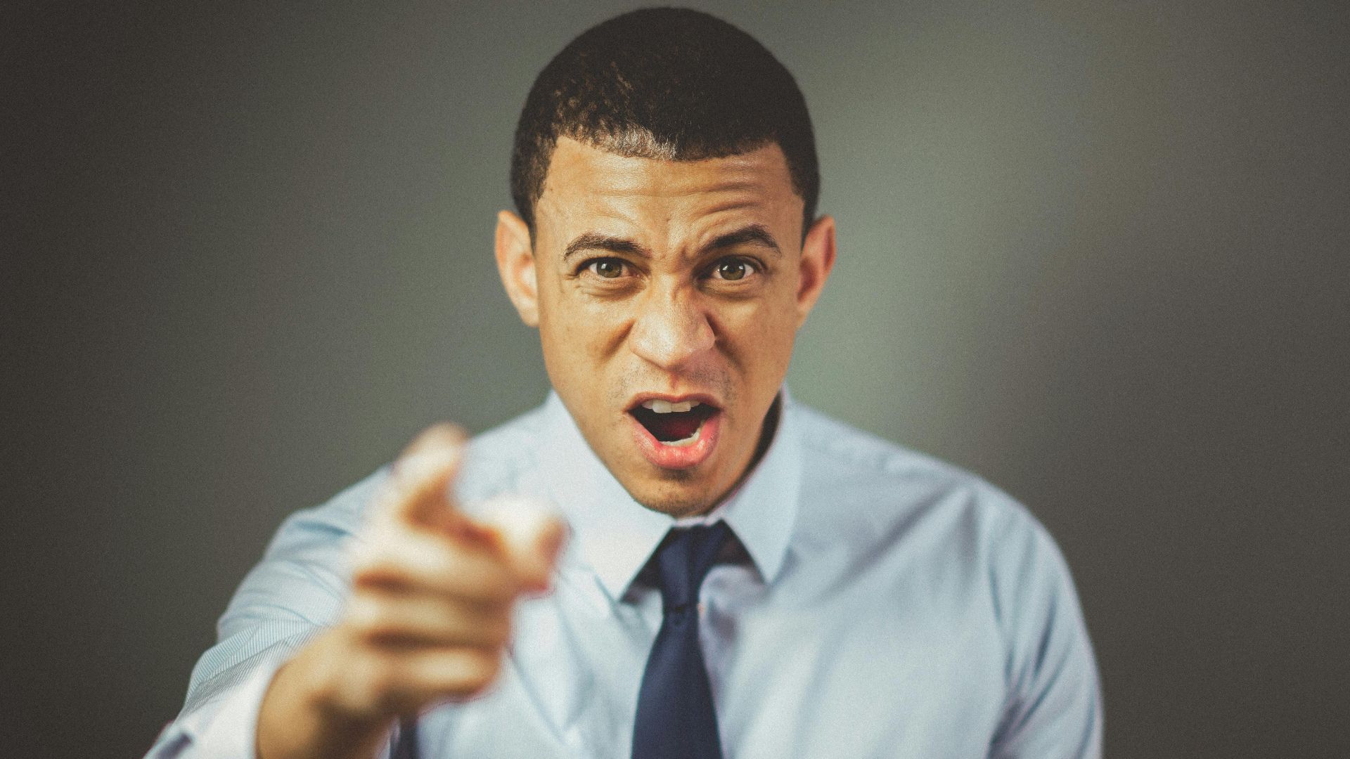 Close-up of an angry businessman in a tie expressing frustration and pointing.