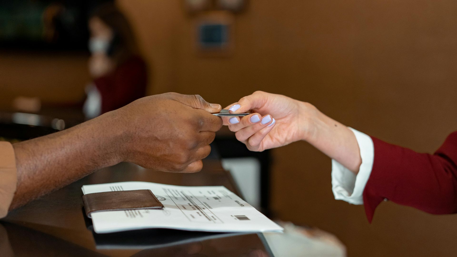 Close-up of a hotel receptionist receiving a credit card from a guest, highlighting a transaction at check-in.