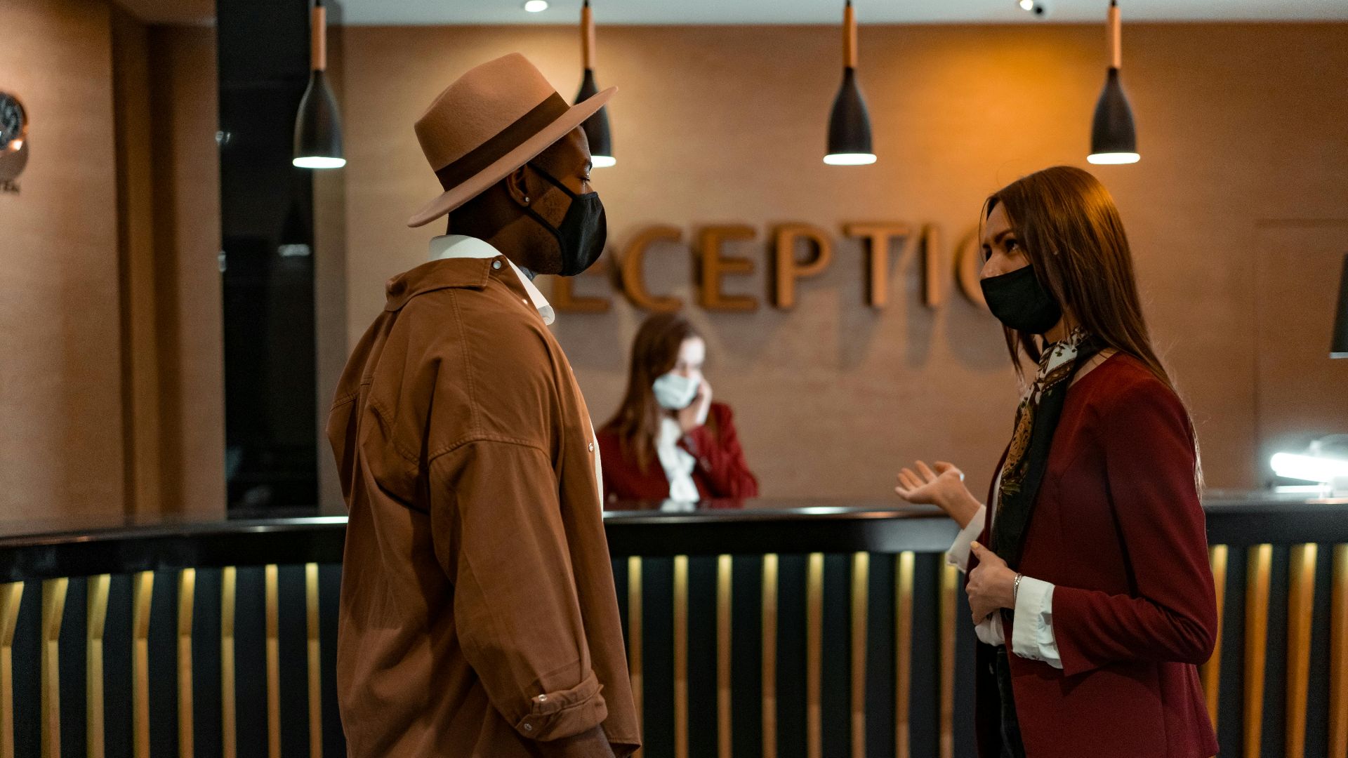 Two people in face masks interacting at a hotel reception desk during the COVID-19 pandemic.