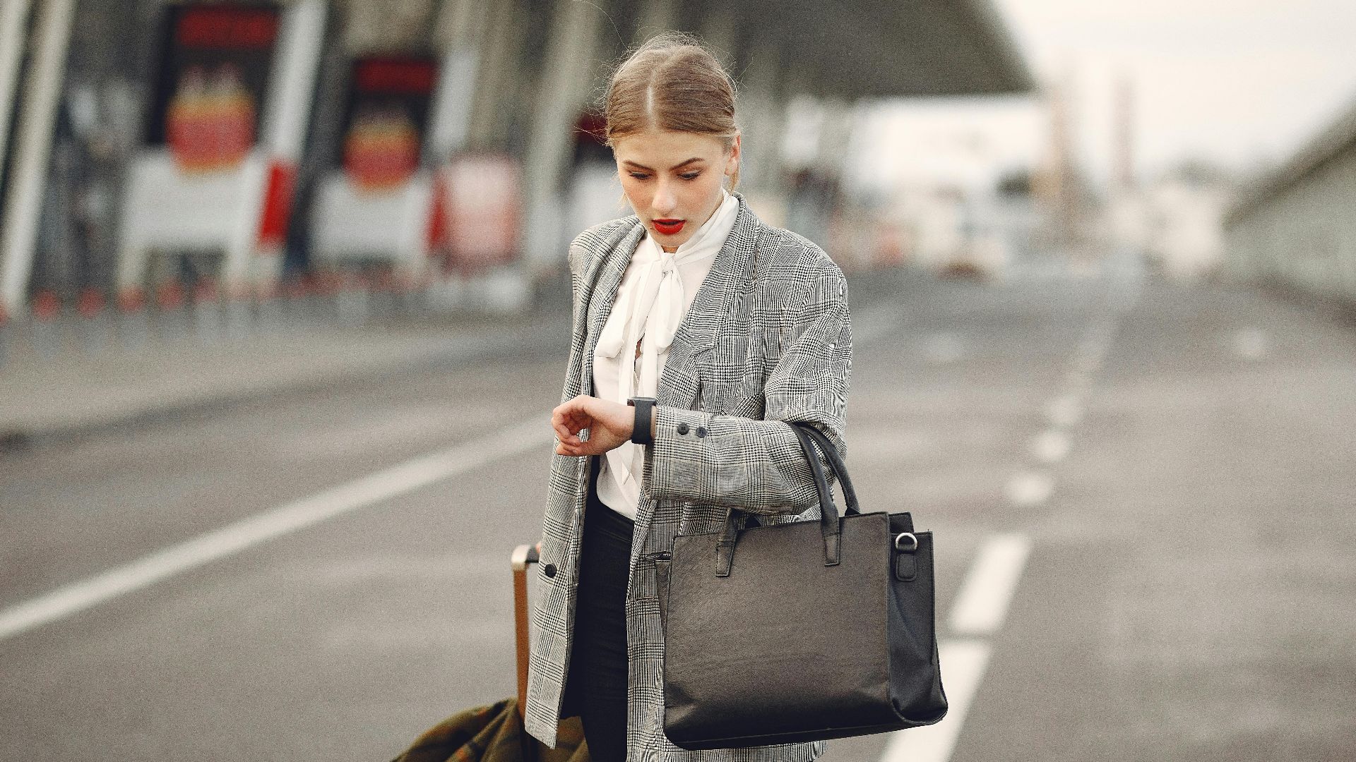 A businesswoman checks her watch while waiting at an airport terminal, looking concerned.