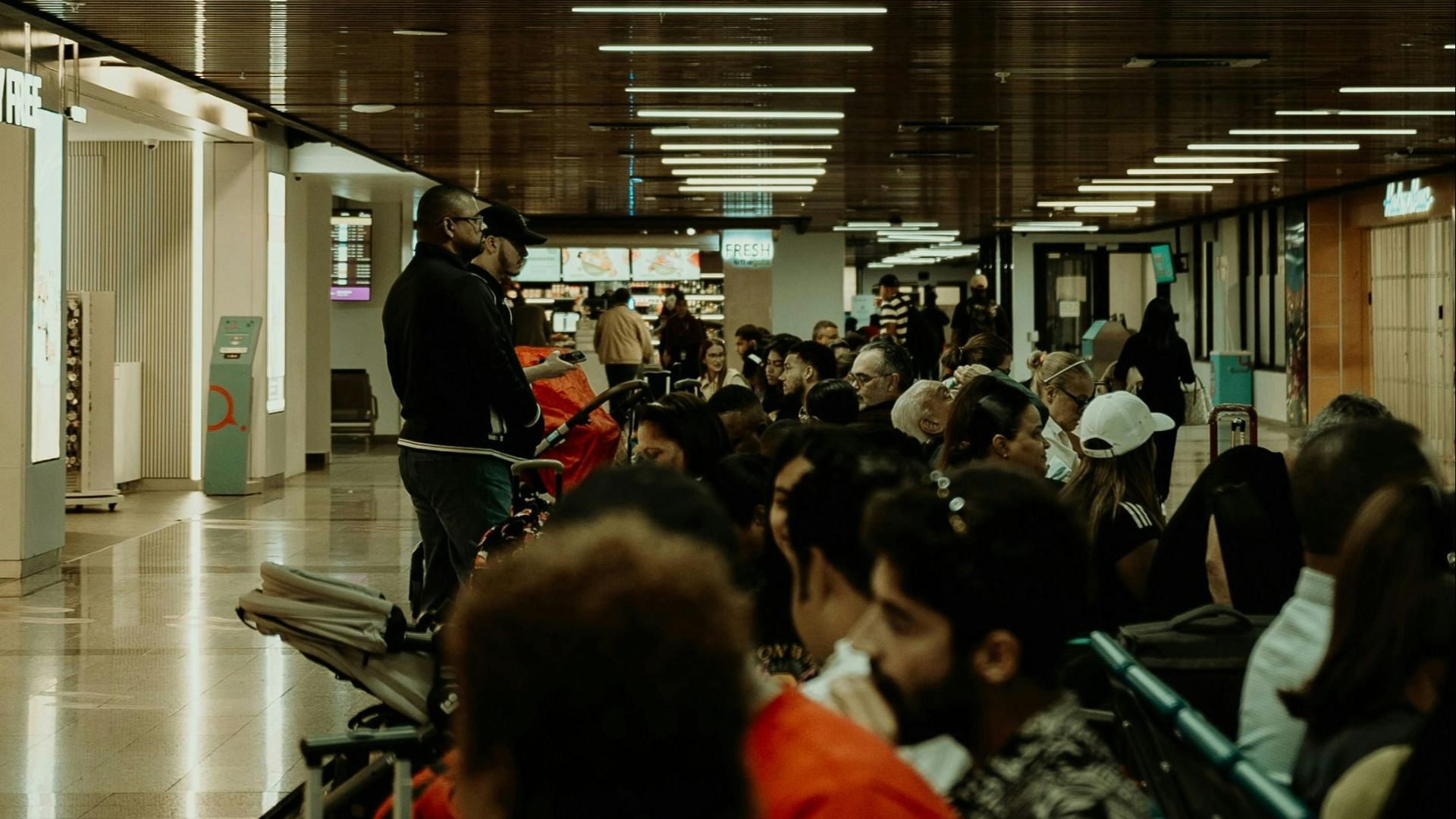 Crowded airport waiting area with diverse passengers seated, waiting for flights.