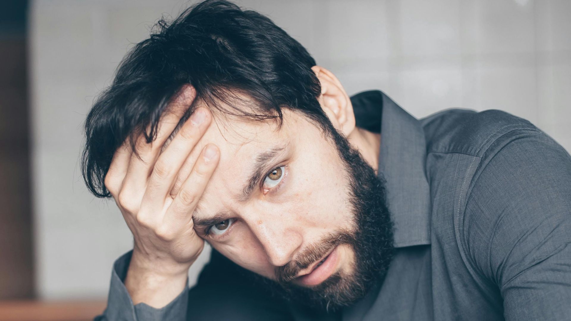 Thoughtful man sitting at a table with glasses and cup, showing frustration.