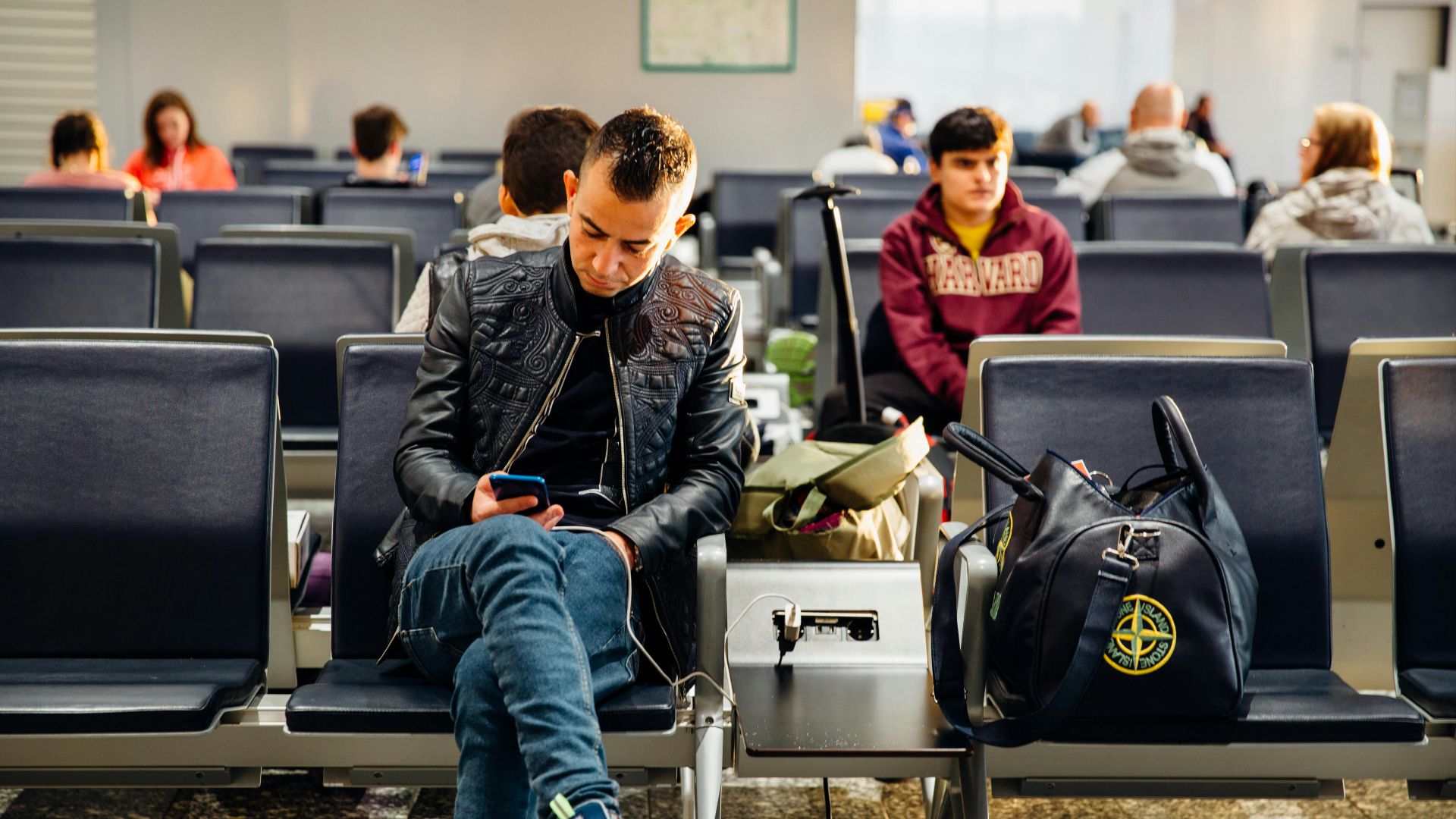 People sitting in an airport lounge, focused on smartphones and waiting for flights.