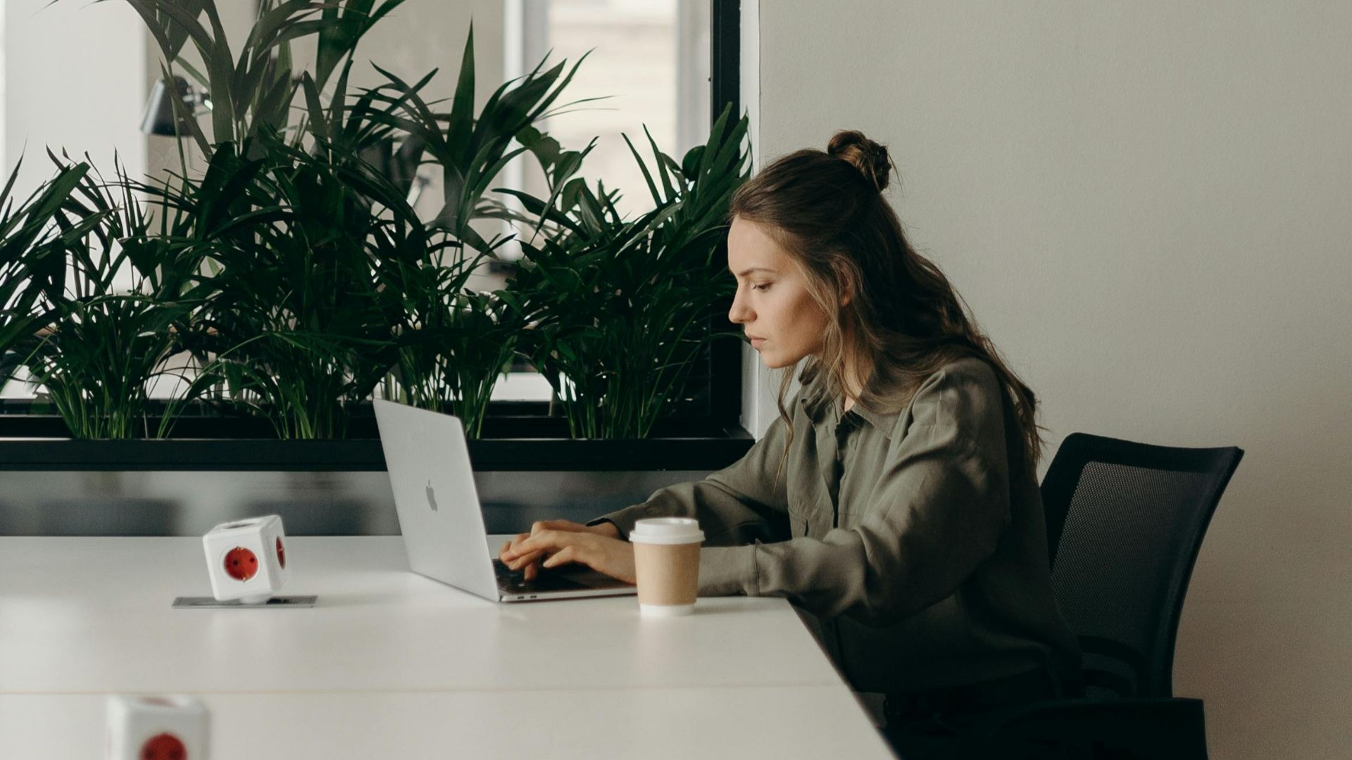 Woman working on a laptop in a minimalist home office with plants.