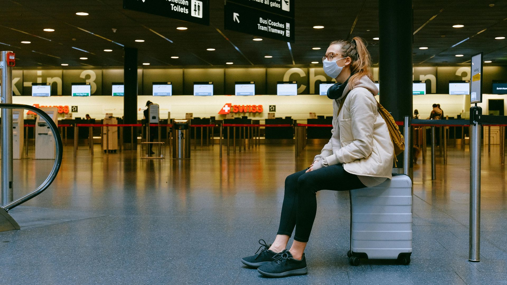 A woman wearing a face mask sits on luggage in an airport terminal amid the pandemic.