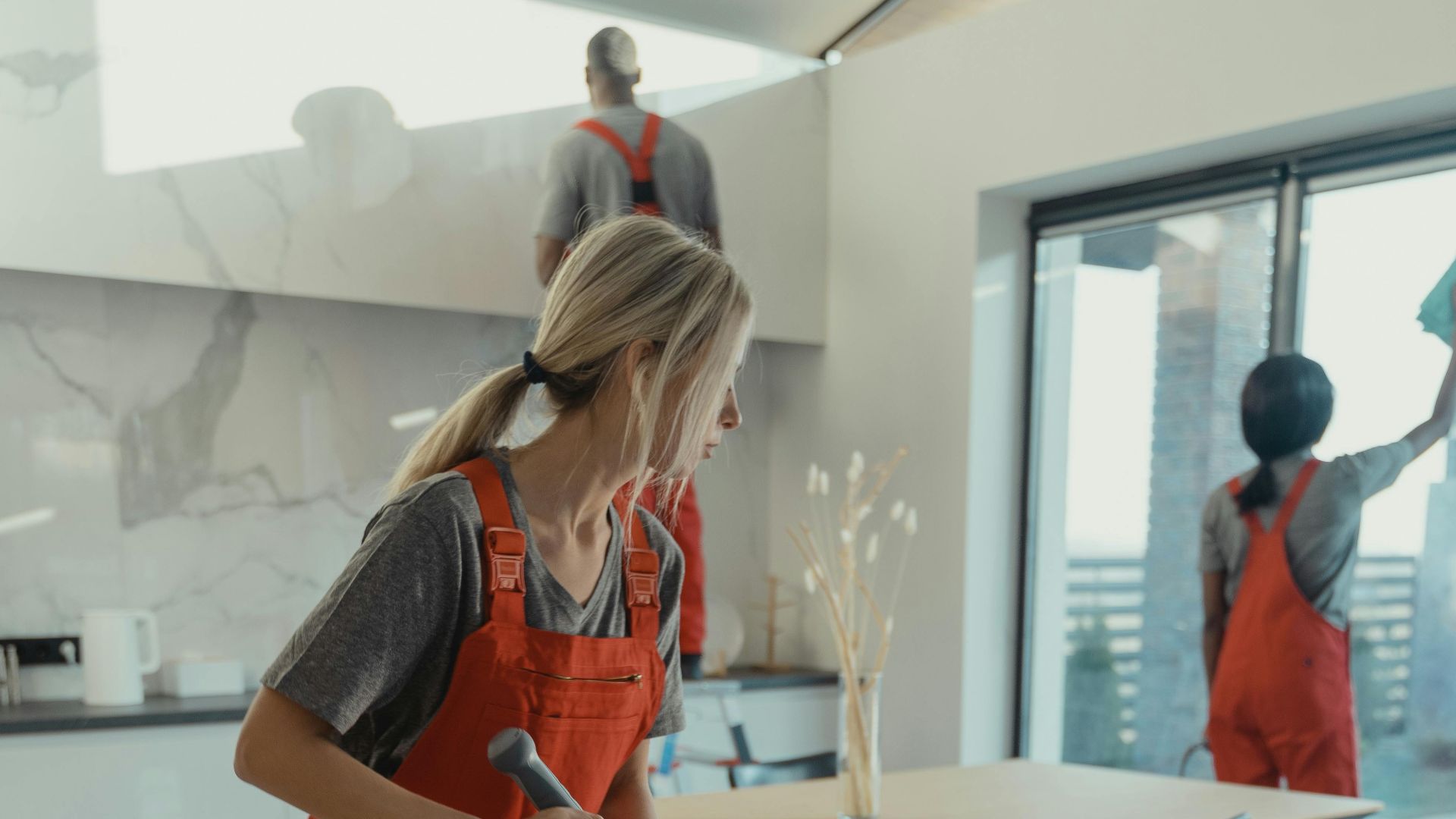 Cleaning team in red overalls mopping and sanitizing a modern home interior.