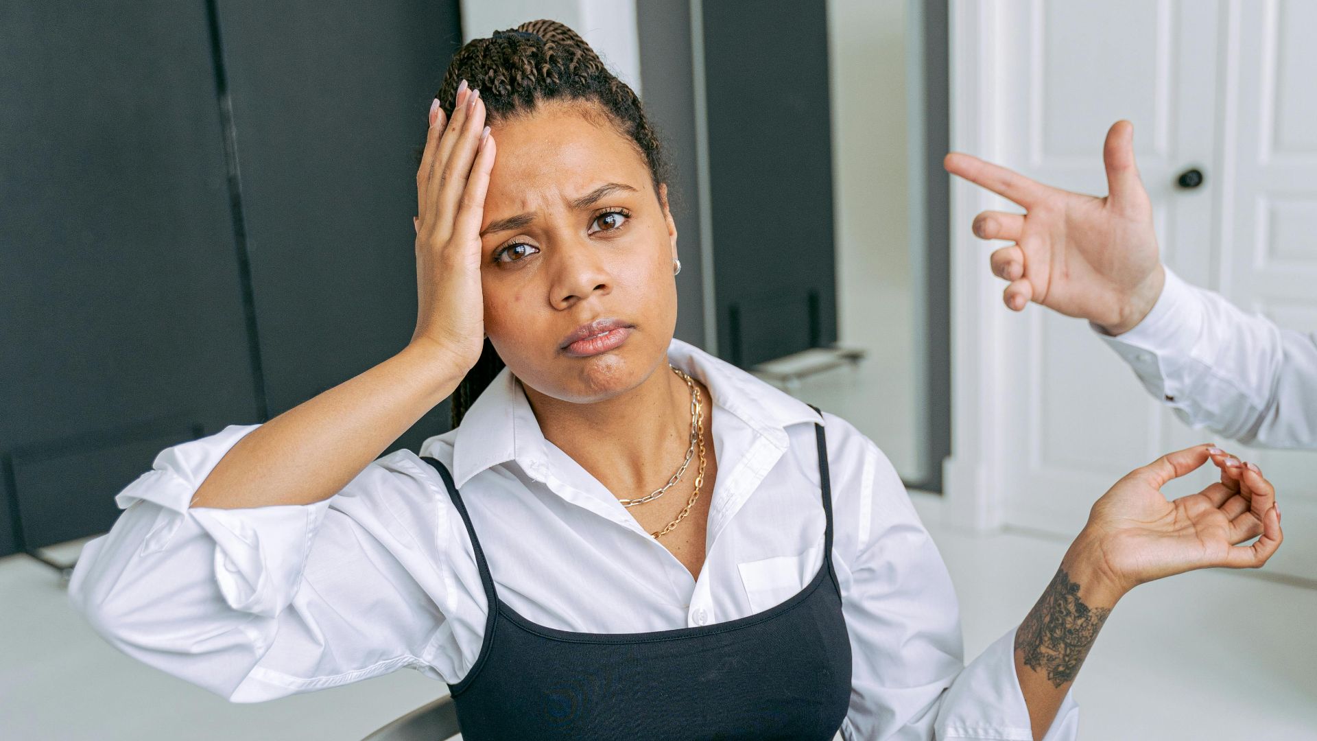 A woman shows confusion as a hand gestures towards her in an office setting.