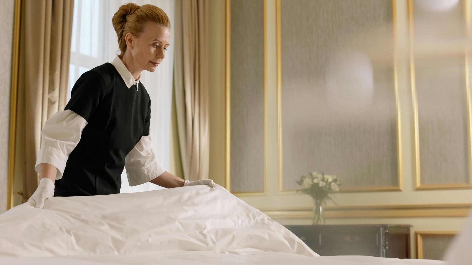 A professional housekeeper fixes a bed in a luxurious hotel room.