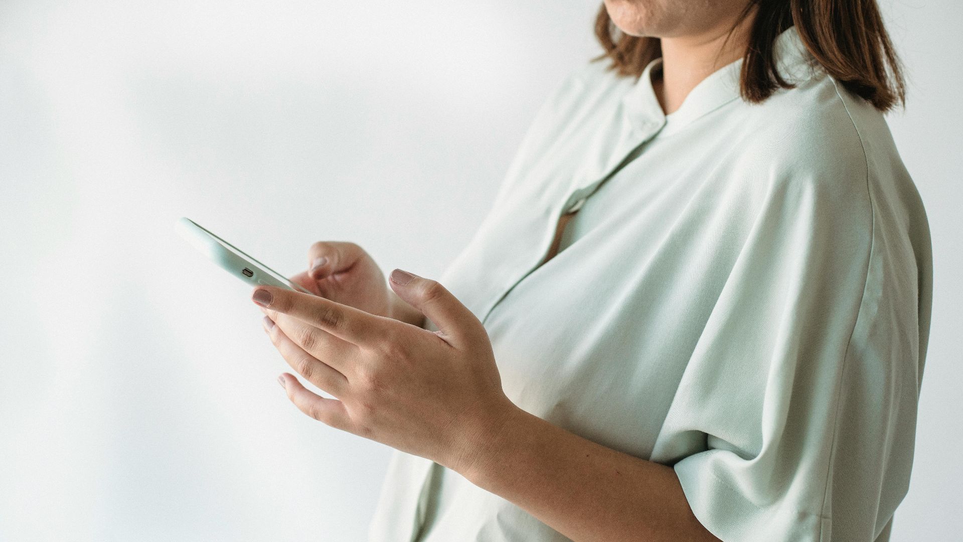 A woman in a light shirt using a smartphone indoors, focus on technology interaction.