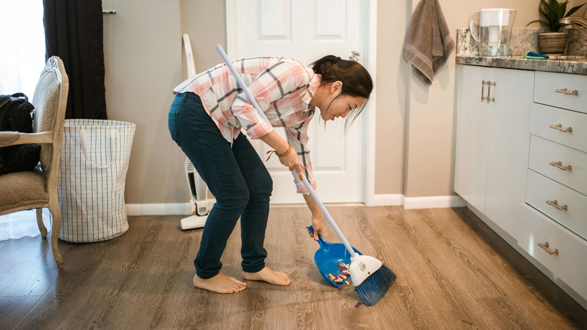 An Asian woman performing cleaning chores by sweeping the floor indoors.