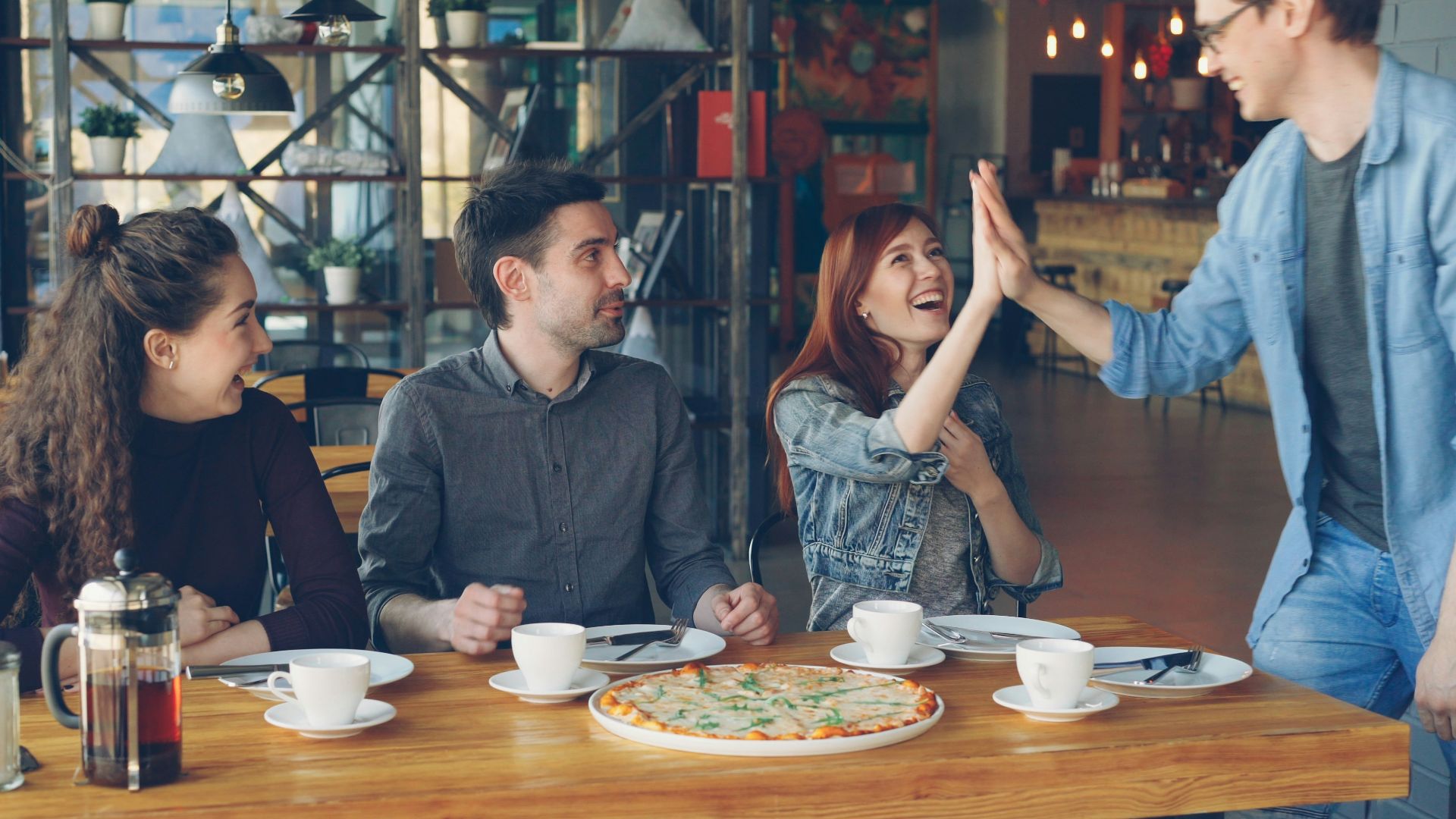 Friends celebrate with a high five over a pizza.