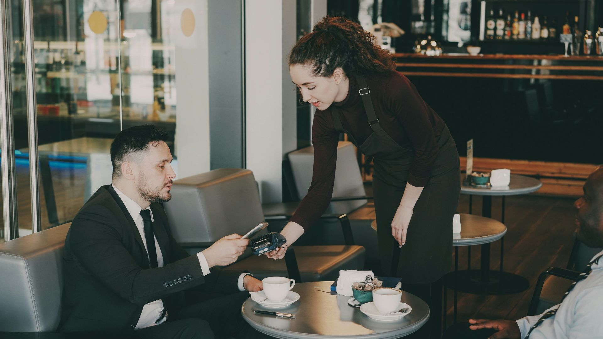 A woman serves coffee to a man in a cafe.