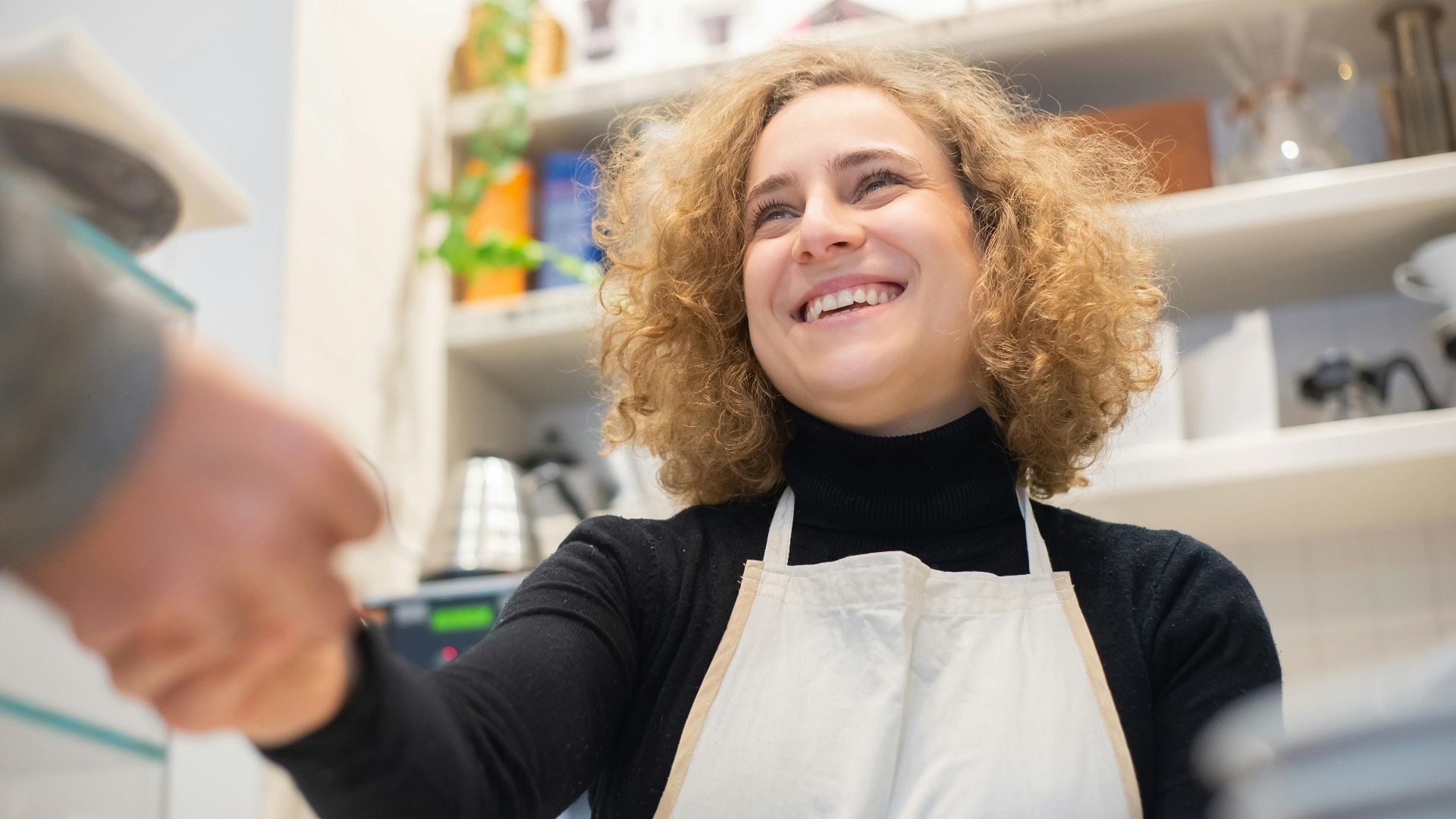 Smiling barista in café, engaging positively with customer, signifying hospitality.