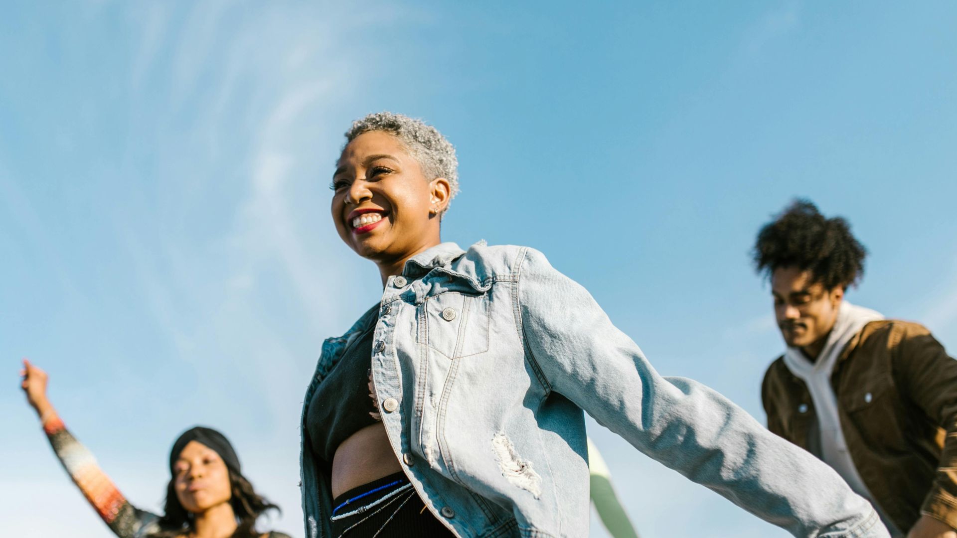 Group of diverse friends dancing outdoors in denim clothing under a clear summer sky.