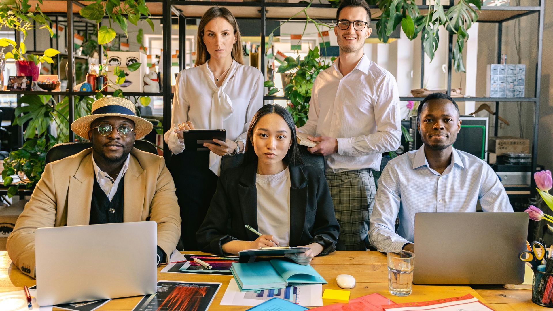 A diverse group of professionals engaged in a collaborative business meeting in a plant-filled modern office setting.