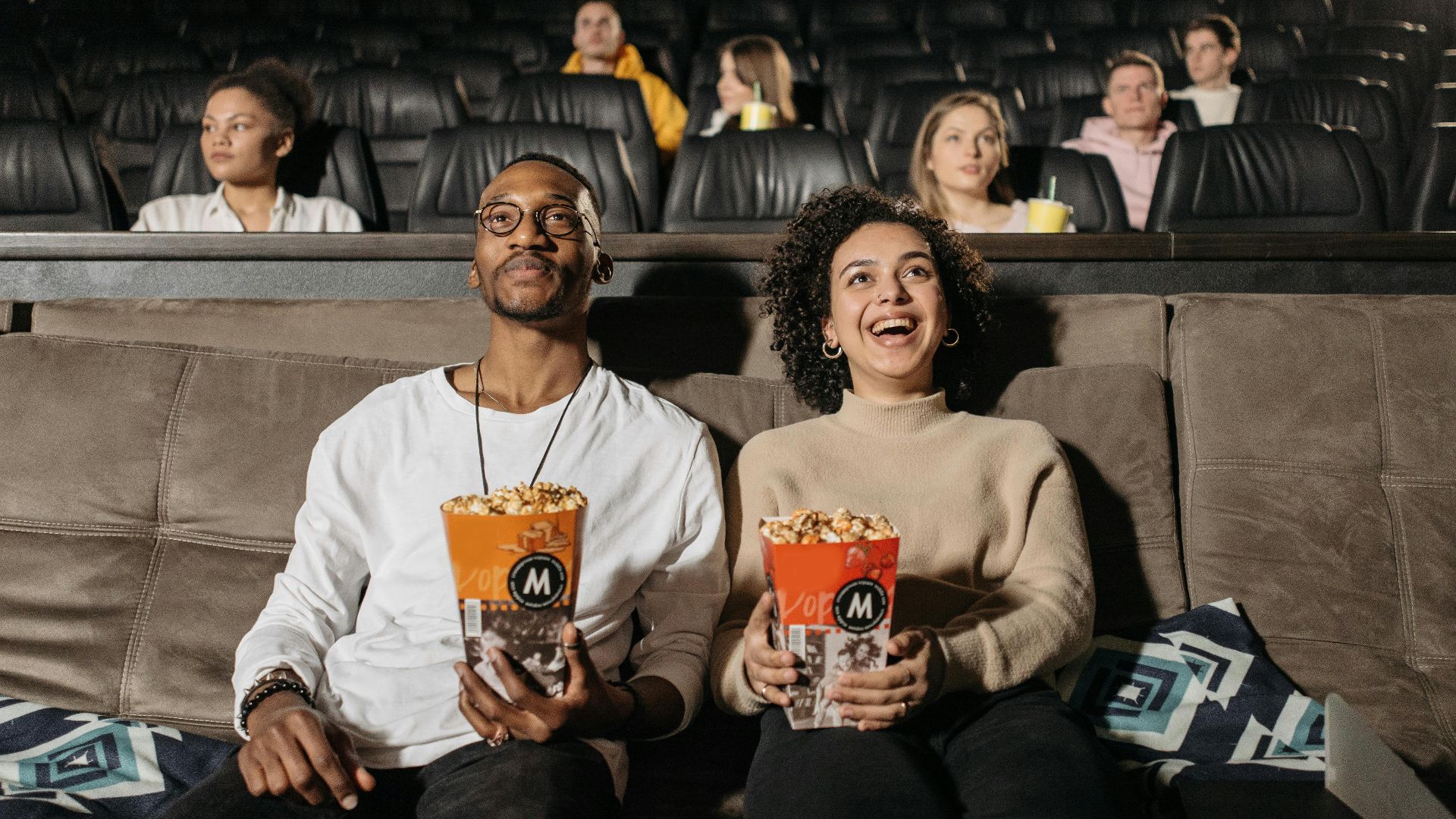 A cheerful couple watching a movie in a cinema, sharing a fun moment with popcorn.